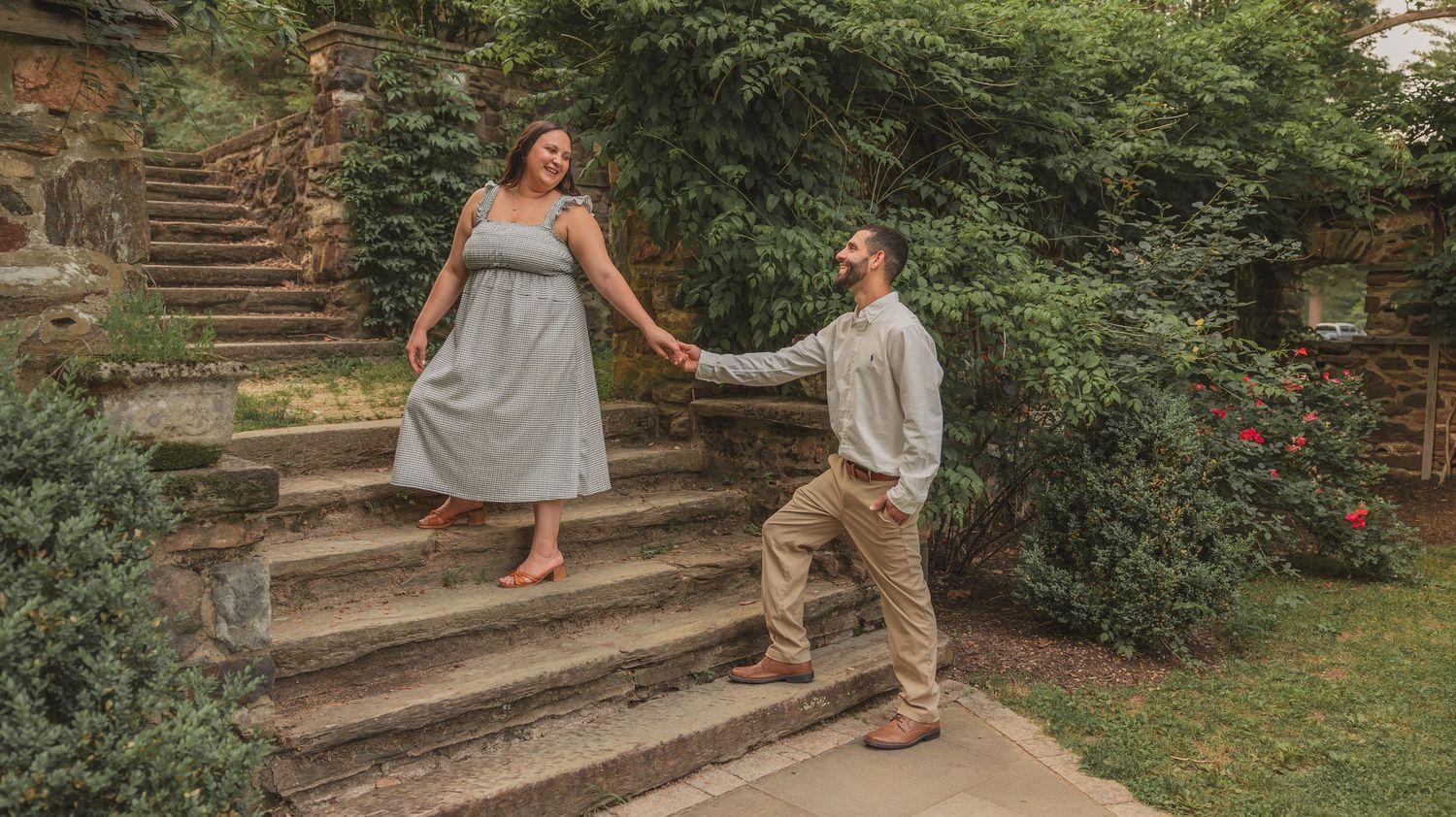 Family sits together on rustic stone steps in a lush garden setting filled with greenery and blooming flowers.