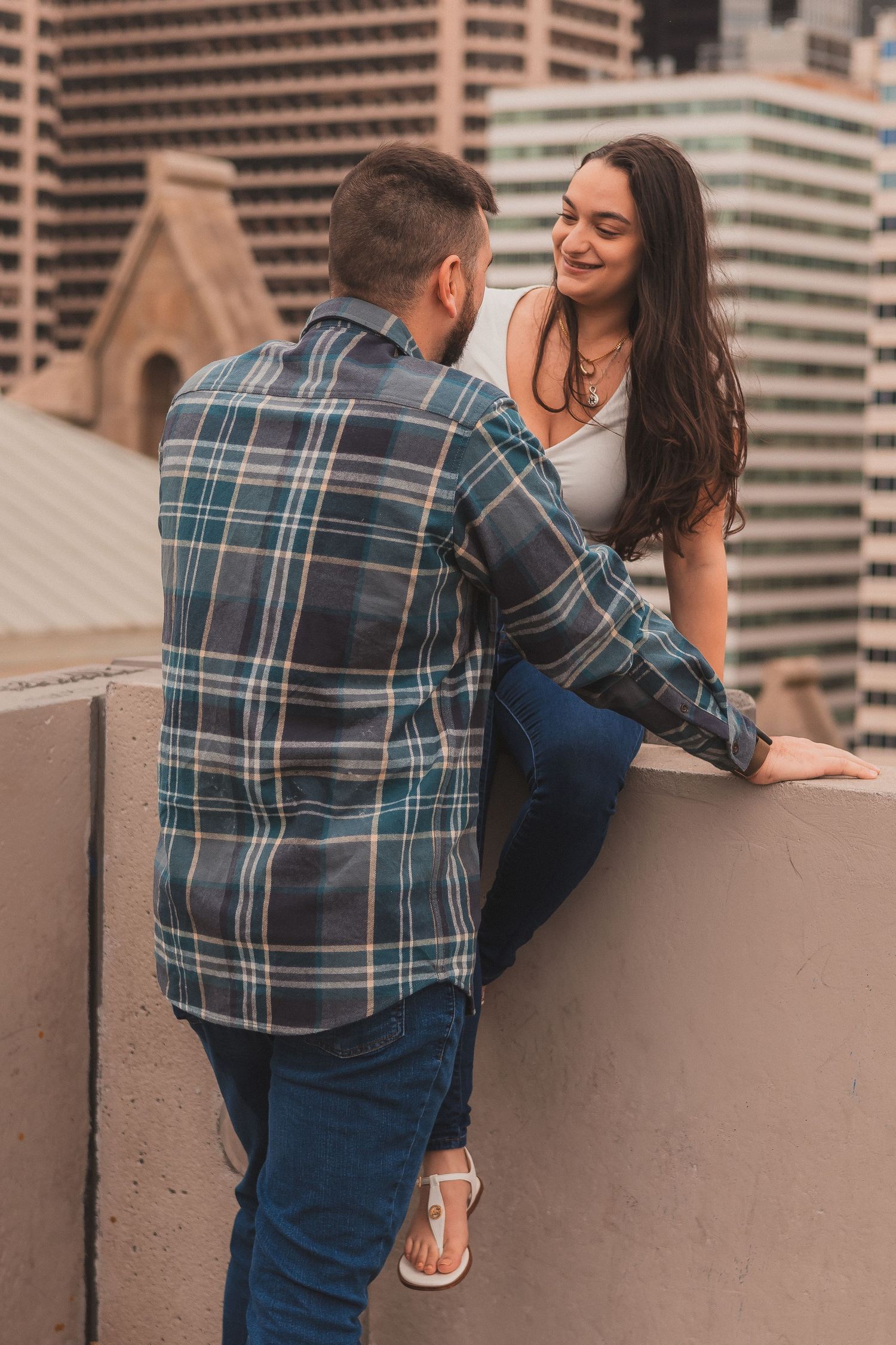A couple sharing a casual moment on an urban rooftop with city buildings in the background.