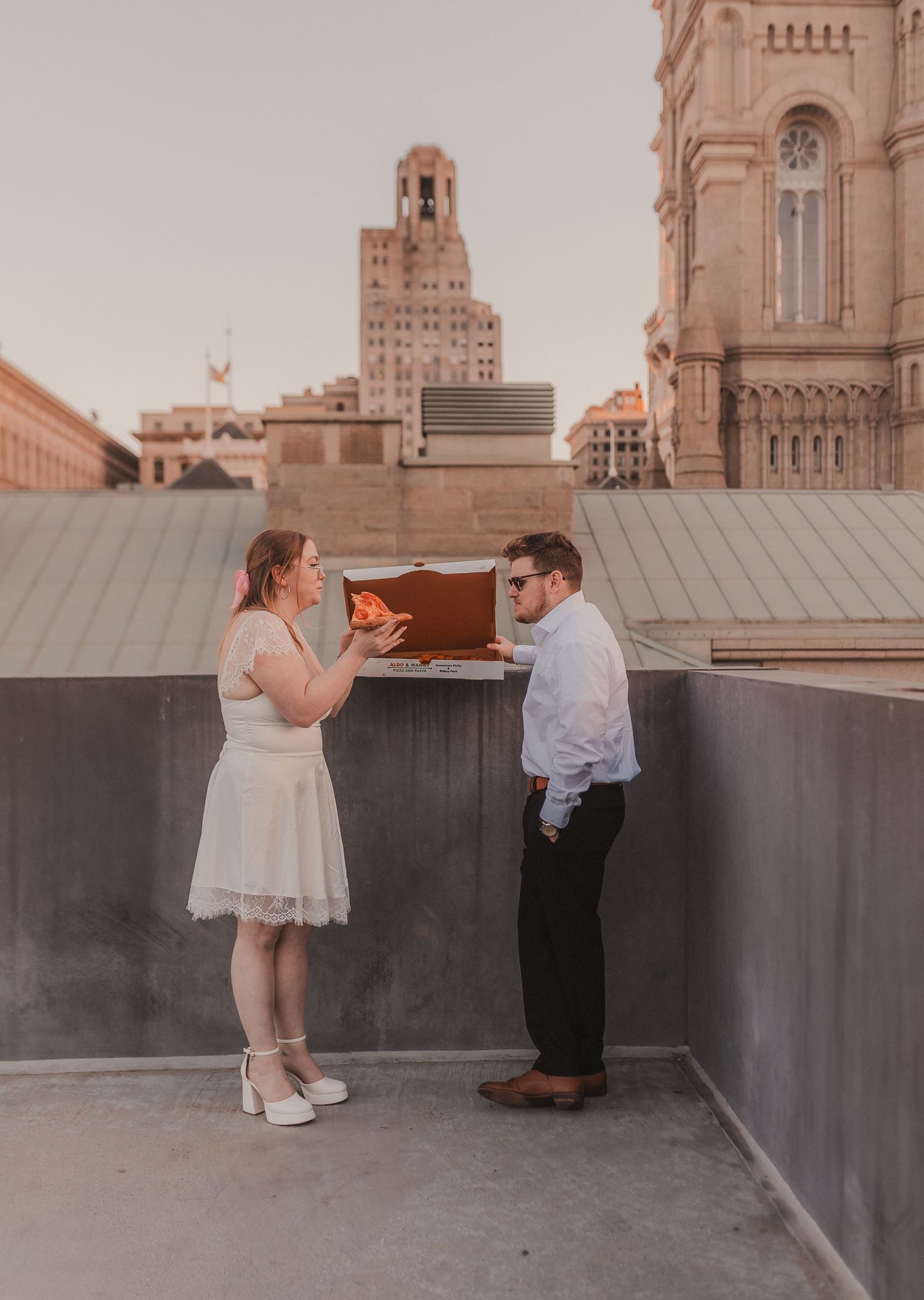 Couple shares pizza on an urban rooftop with historic architecture in the background.