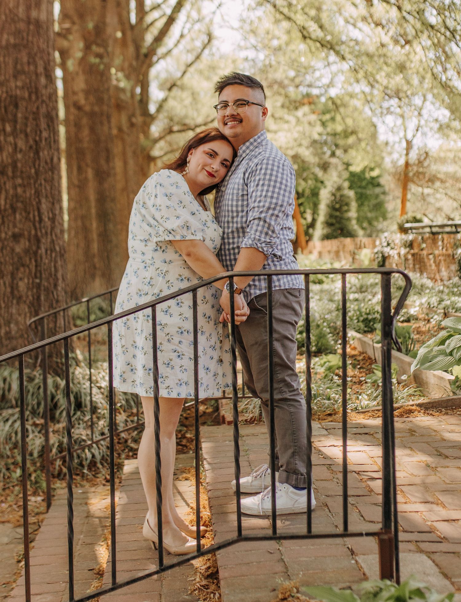 A couple embraces on garden steps while leaning against black iron railings.