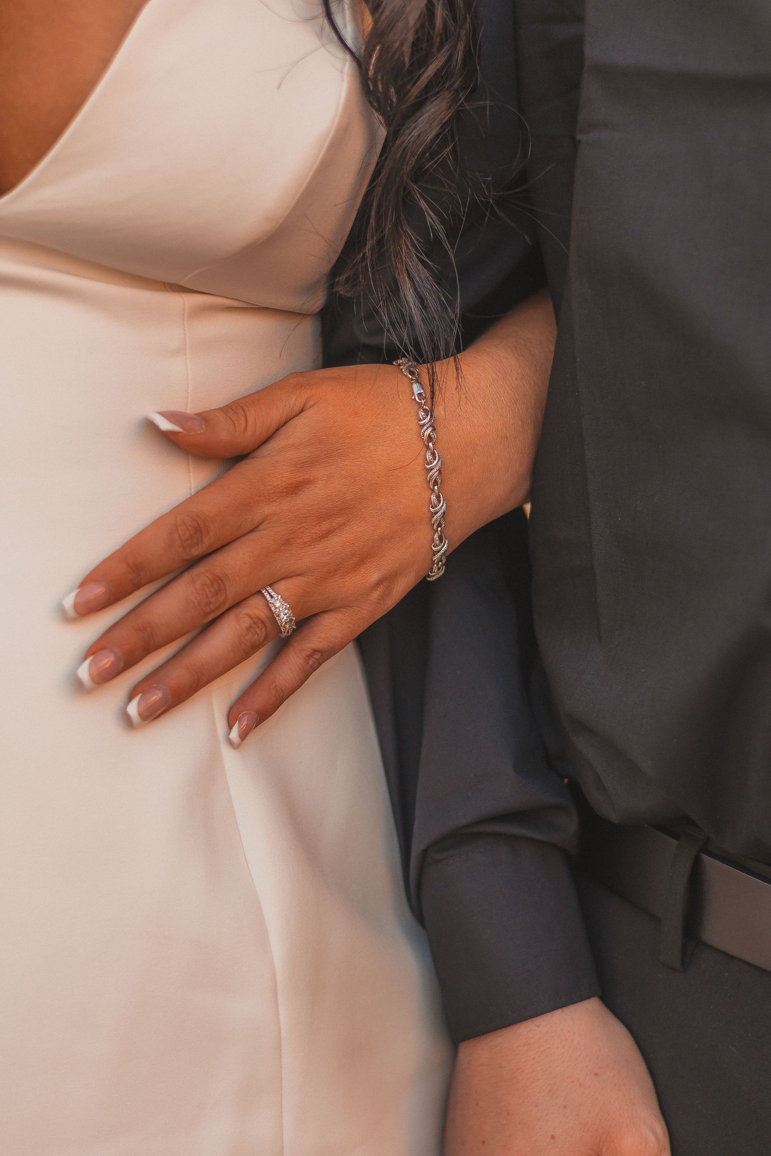 A close-up shot of hands showing off wedding rings and jewelry against formal attire.