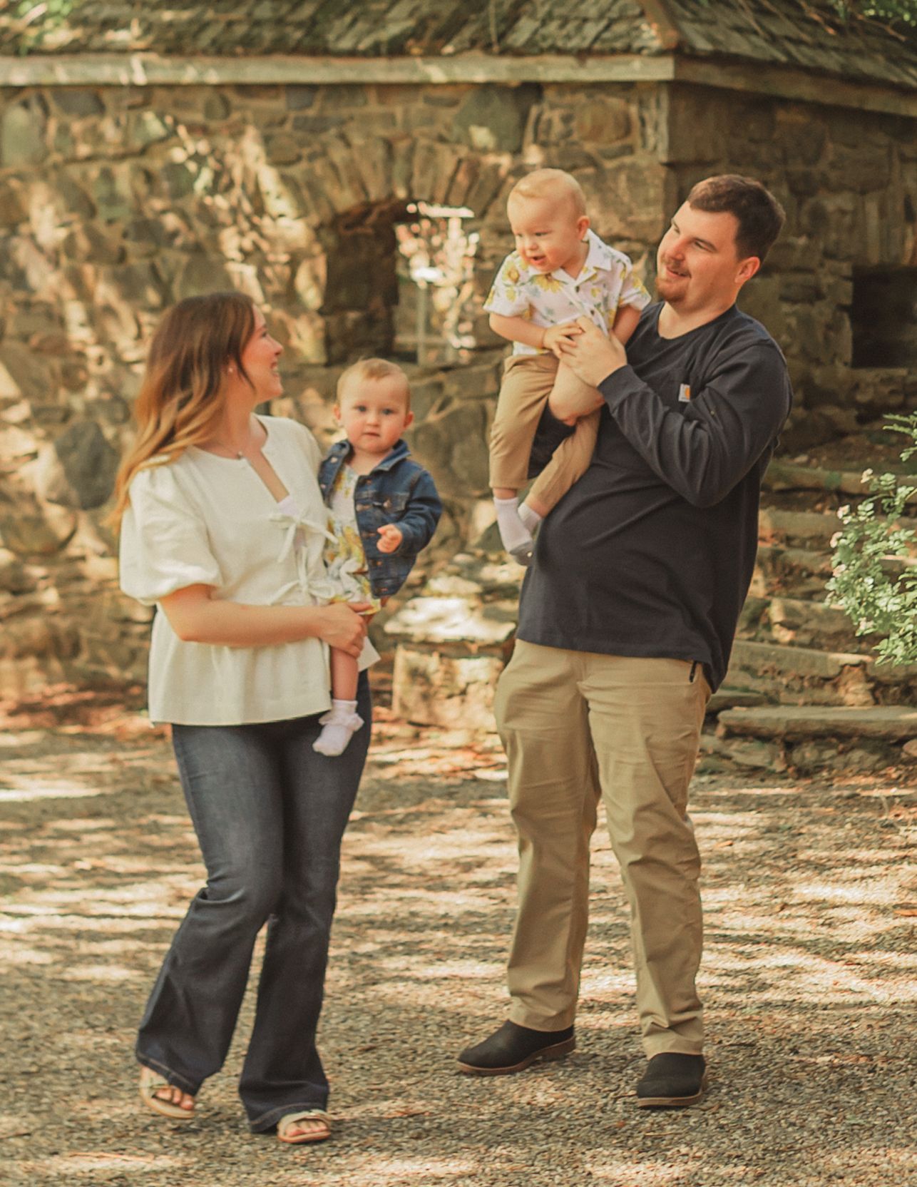A family poses together outdoors in front of a stone wall on a sunny autumn afternoon.