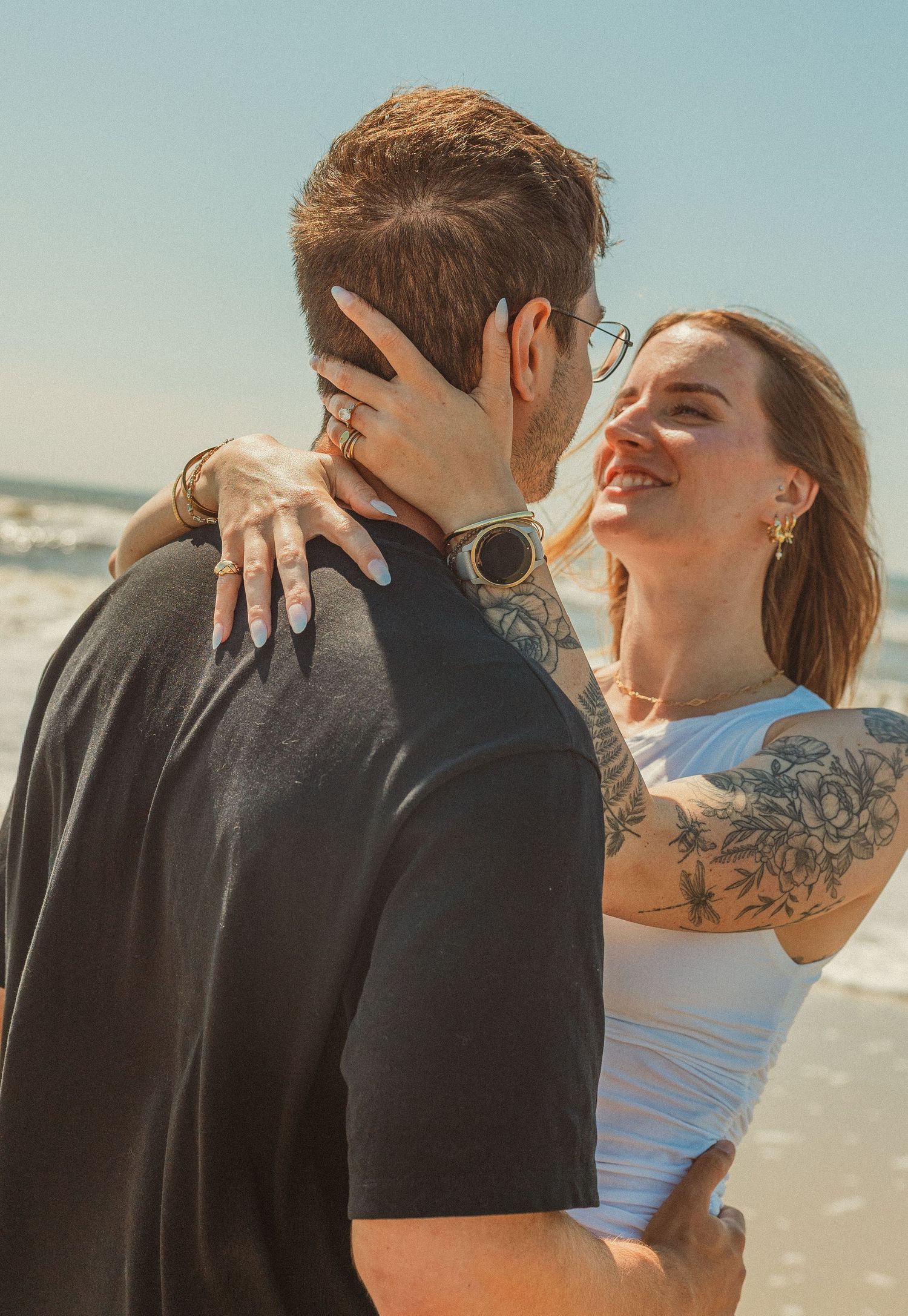 A couple embraces intimately on a beach, silhouetted against a bright coastal backdrop.