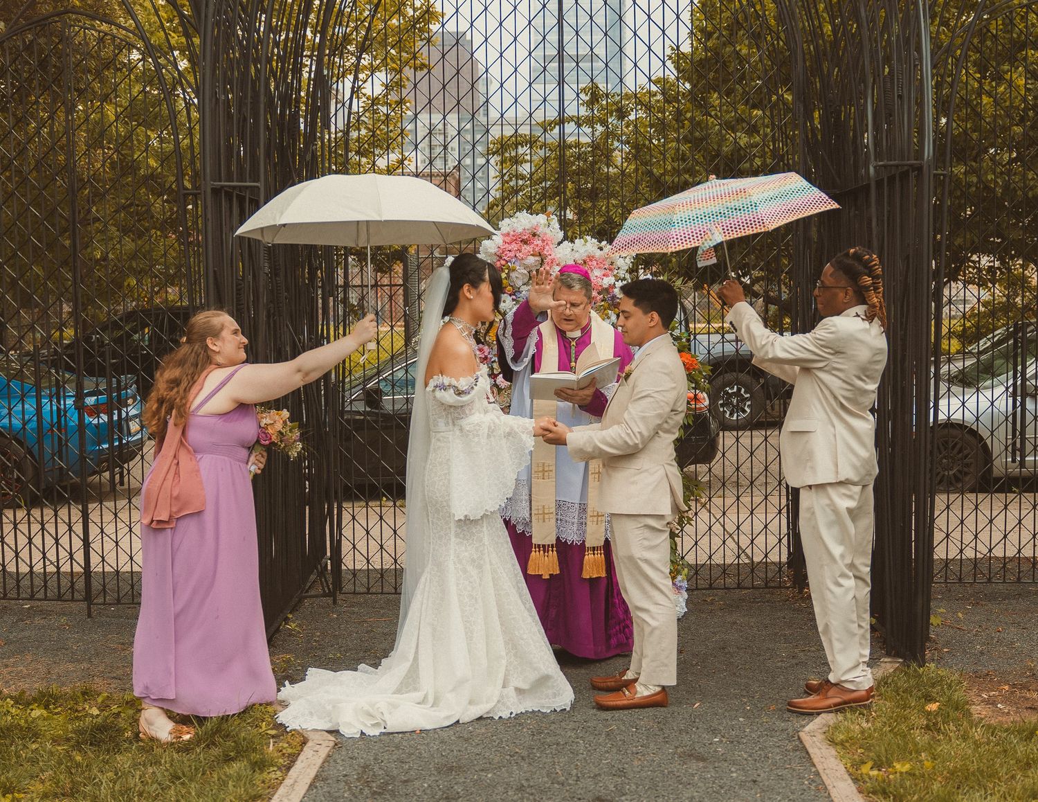 Wedding party members hold umbrellas over a couple during an autumn outdoor ceremony with fall foliage.