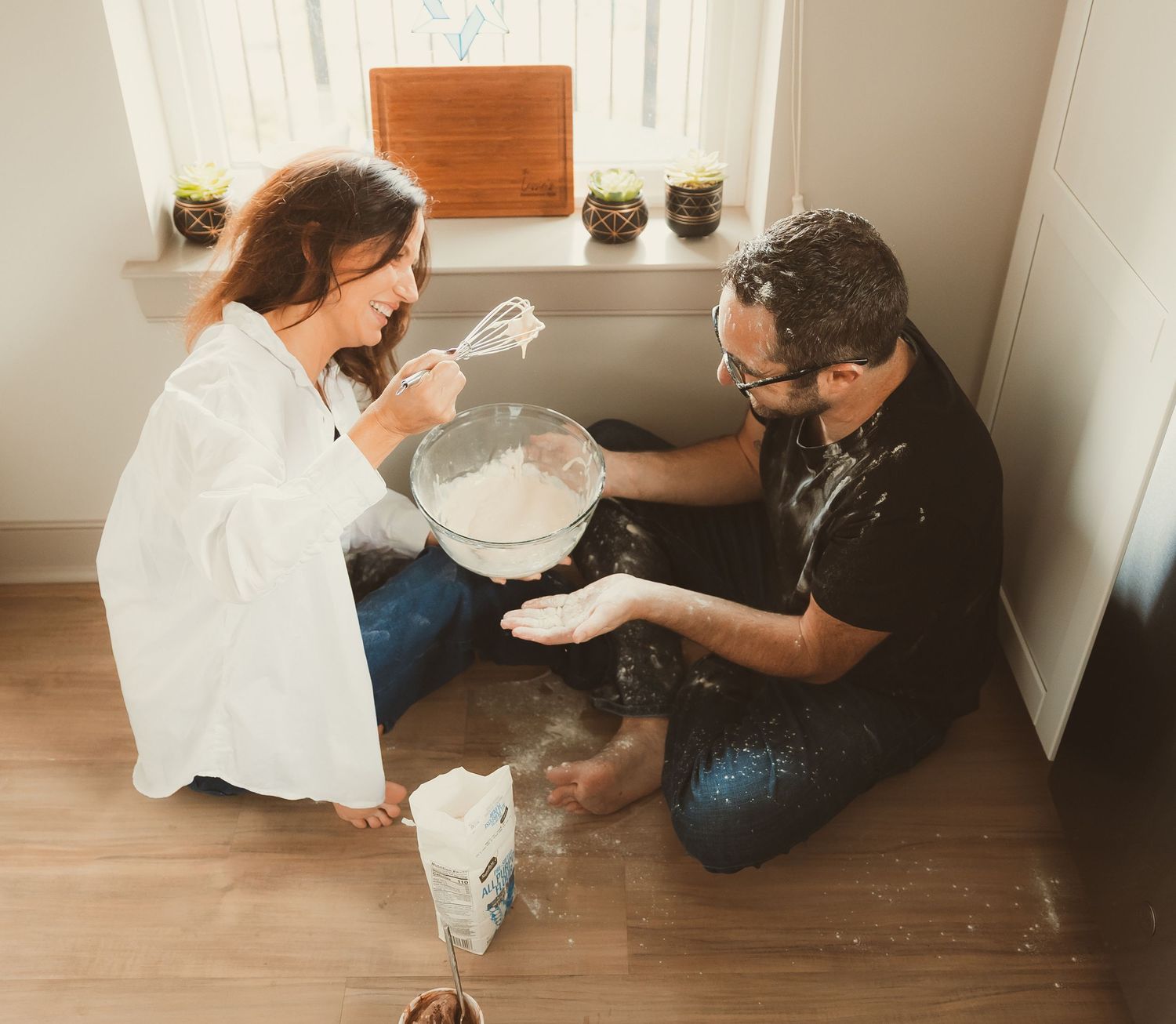 Couple sitting on wooden floor with paint supplies sharing an intimate moment while working on a home improvement project.
