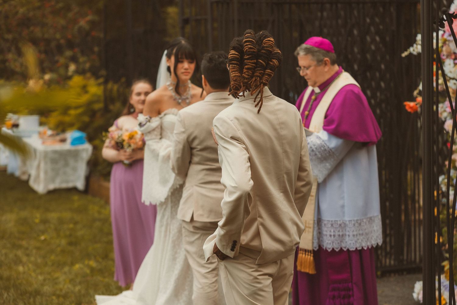 Wedding guests gather outdoors under tall trees at an autumn ceremony with warm lighting and elegant decor.