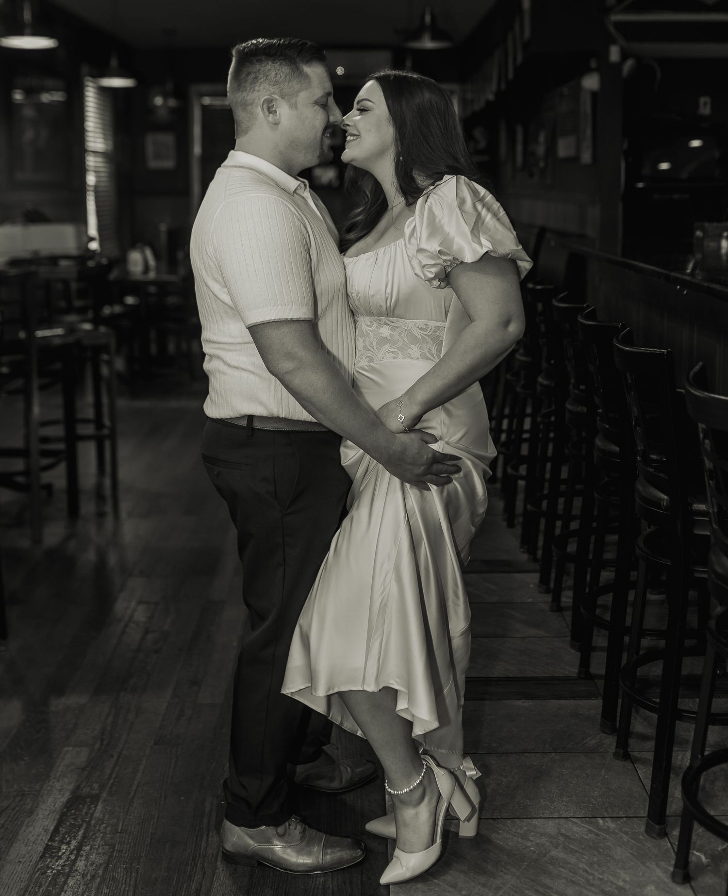 A romantic vintage black and white photograph of a couple dancing together in an empty bar with hardwood floors.