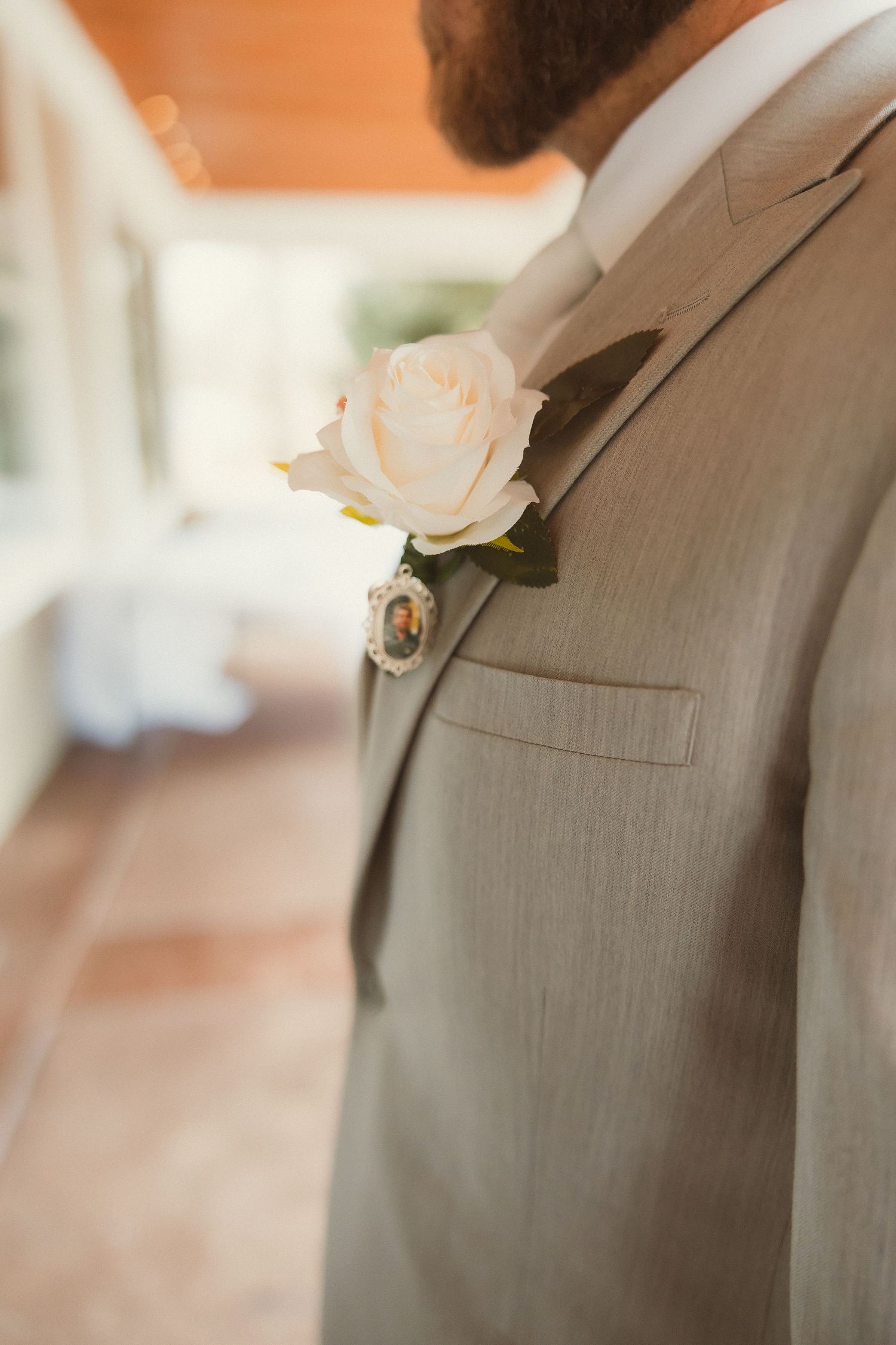 A delicate white rose boutonniere pinned to a light gray suit jacket lapel.