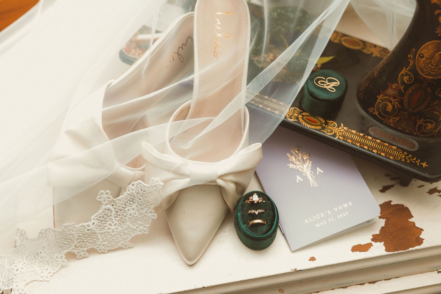 A pair of deep green vintage leather shoes sits beside delicate white lace and sheer fabric on a wooden surface.