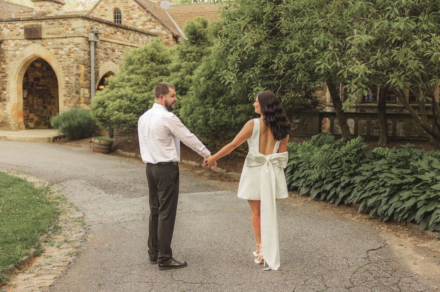 A romantic couple holds hands and spins together on a stone path near a historic church building.