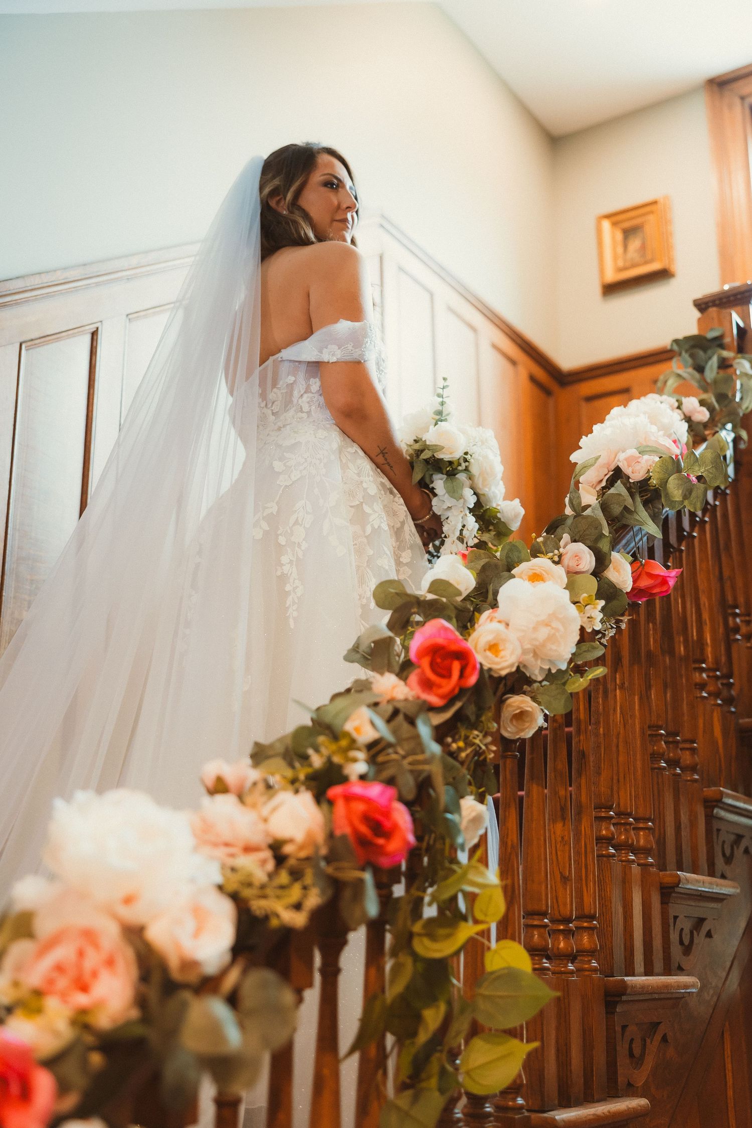 Wedding dress detail on staircase with floral garland featuring coral and white roses.