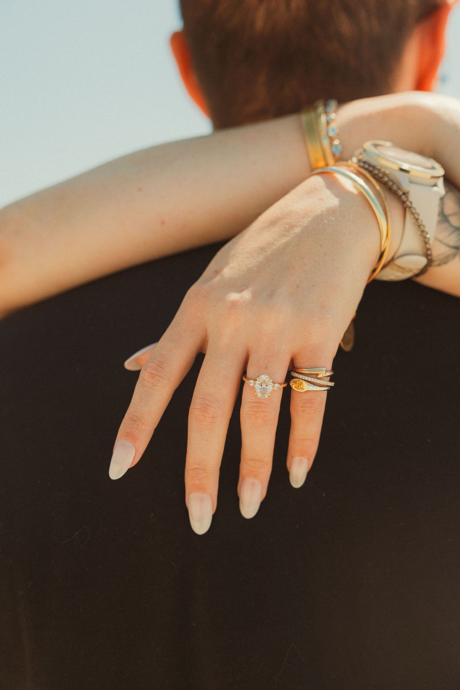 Hand adorned with minimalist gold rings and neutral nail polish displaying modern jewelry styling on dark background.