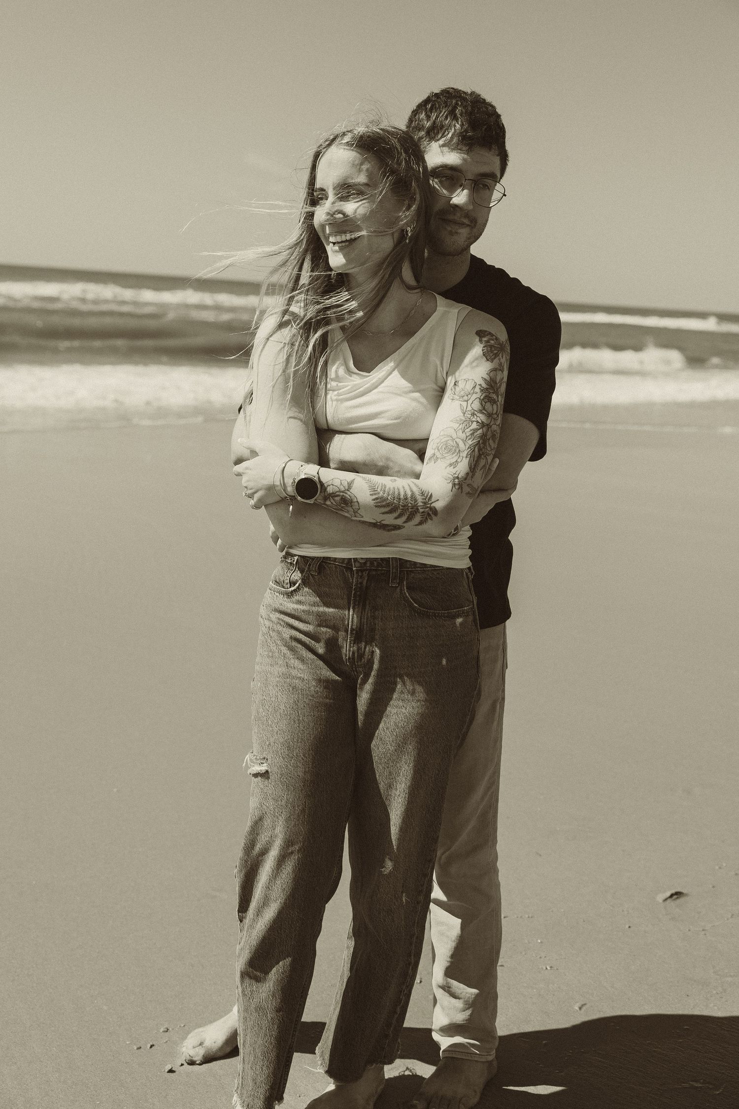 A romantic black and white photo series of a couple playfully interacting together on a sunlit beach.