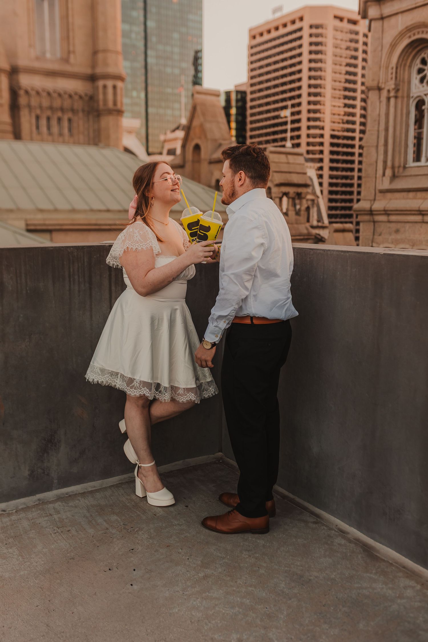 Couple shares a romantic moment on rooftop with sunflowers and urban architecture.