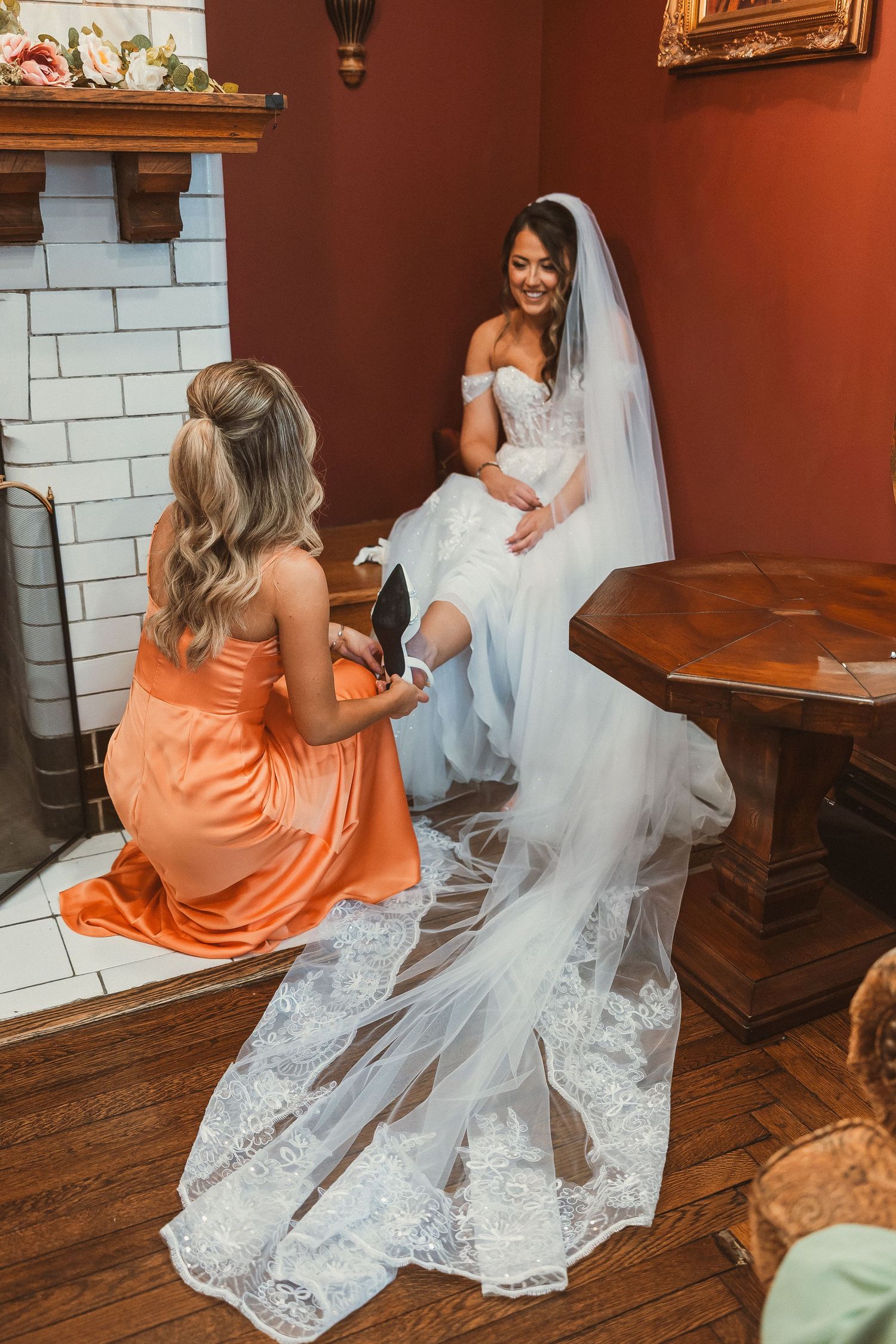Wedding preparation scene with flowing white dress and orange bridesmaid gown in warm-toned room.