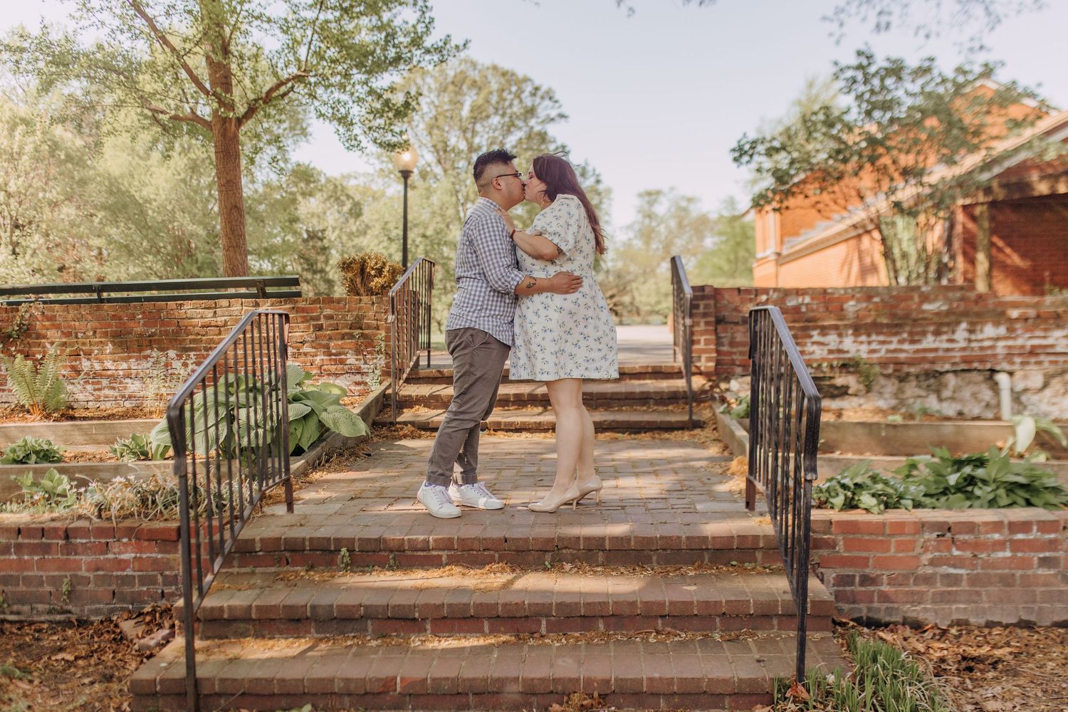 A couple poses on garden steps with black iron railings during an outdoor photoshoot.