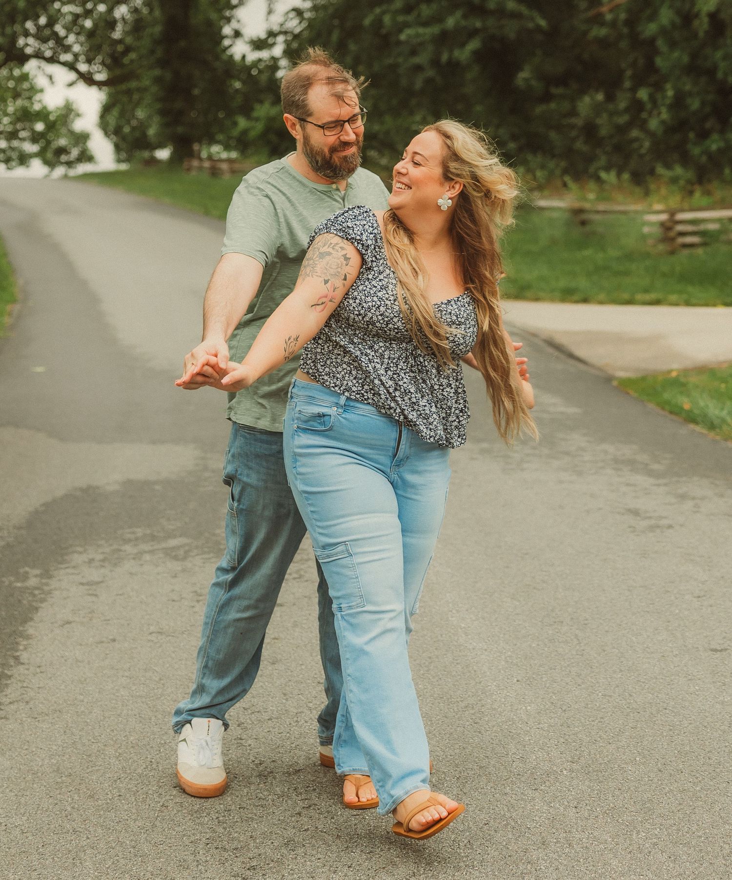 A couple dancing joyfully on a path, with the person in denim leading their partner in blue through playful spins outdoors.