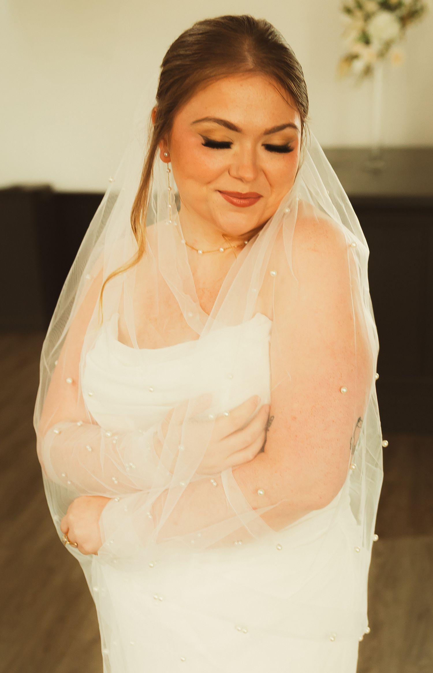 Smiling bride in white wedding dress and veil with soft makeup poses in natural light.