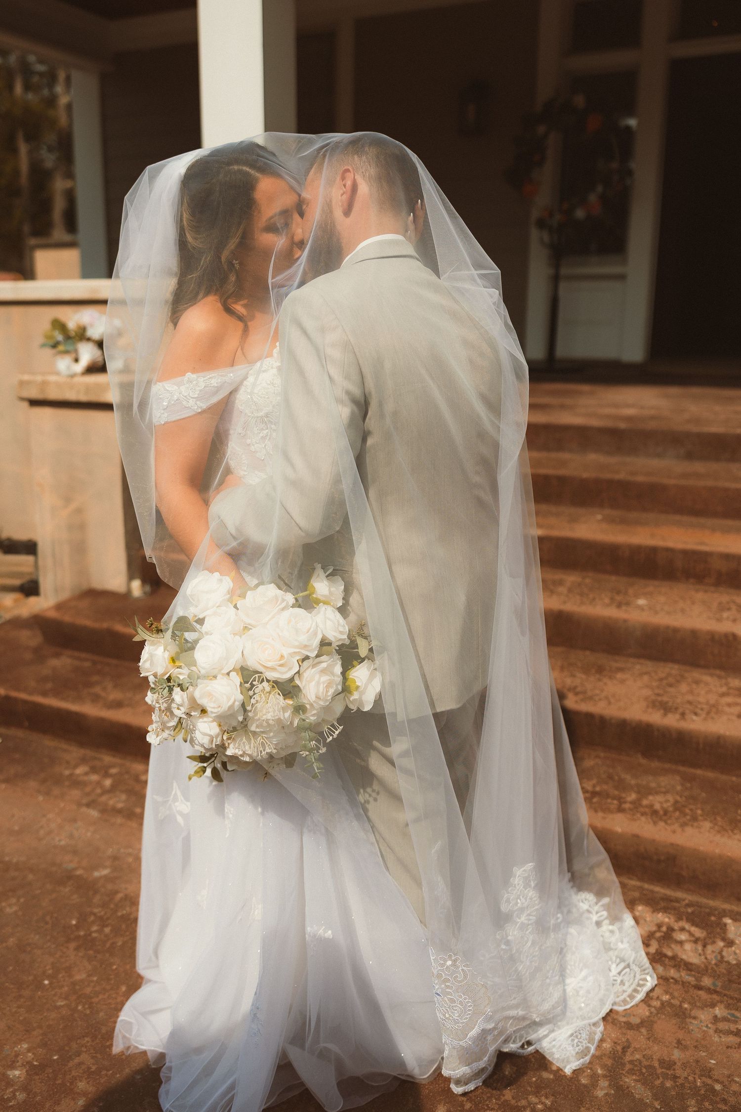A romantic wedding portrait on stairs with the couple sharing an intimate moment under a veil.