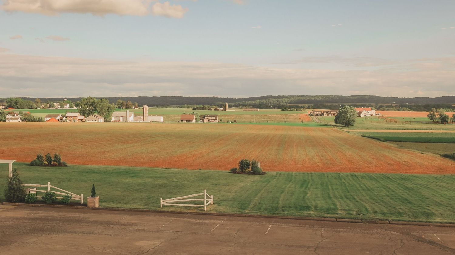 Scenic aerial view of rural farmland with green and golden fields stretching across rolling countryside at sunset.