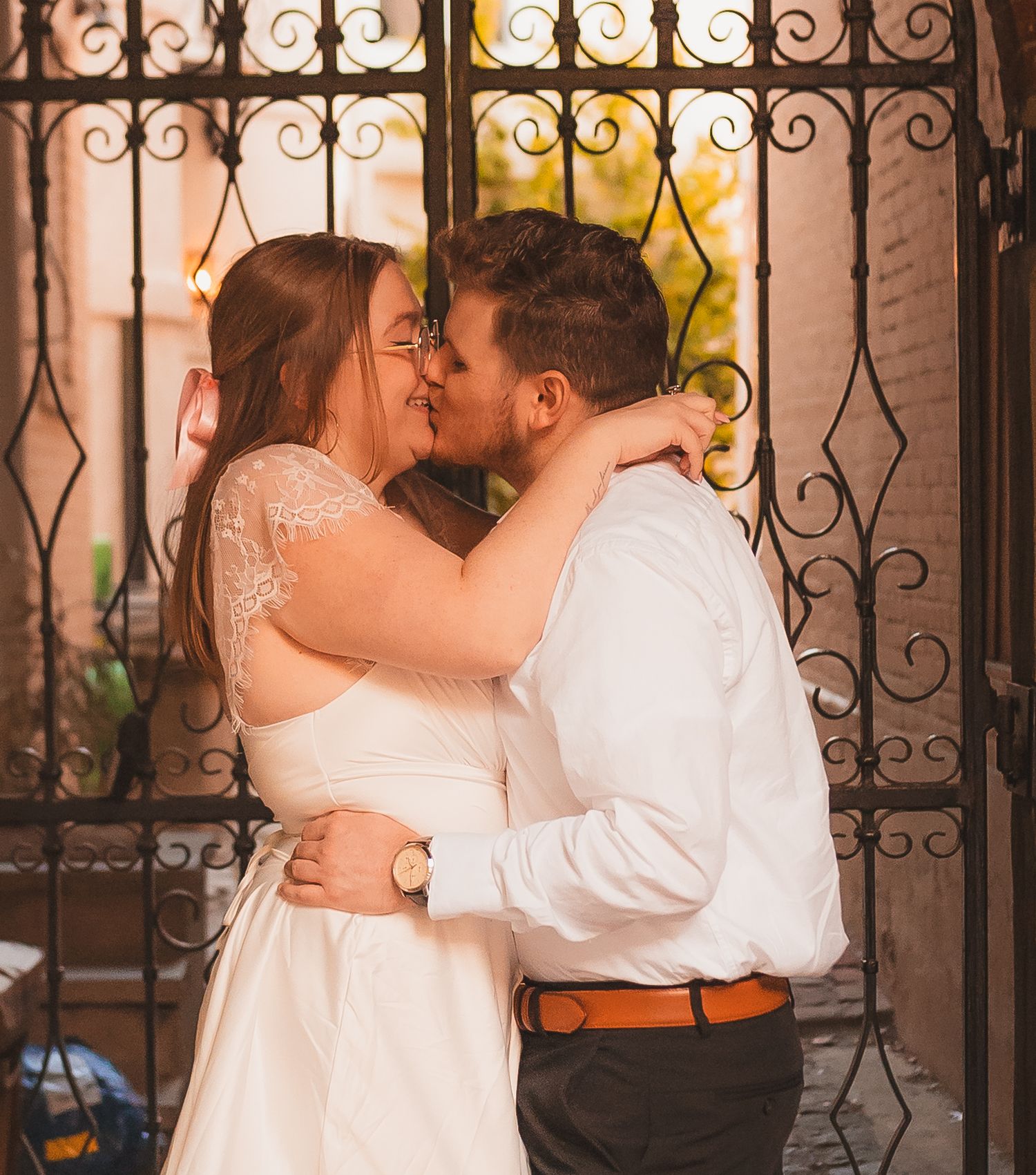 A romantic couple shares an intimate moment against a decorative iron gate.