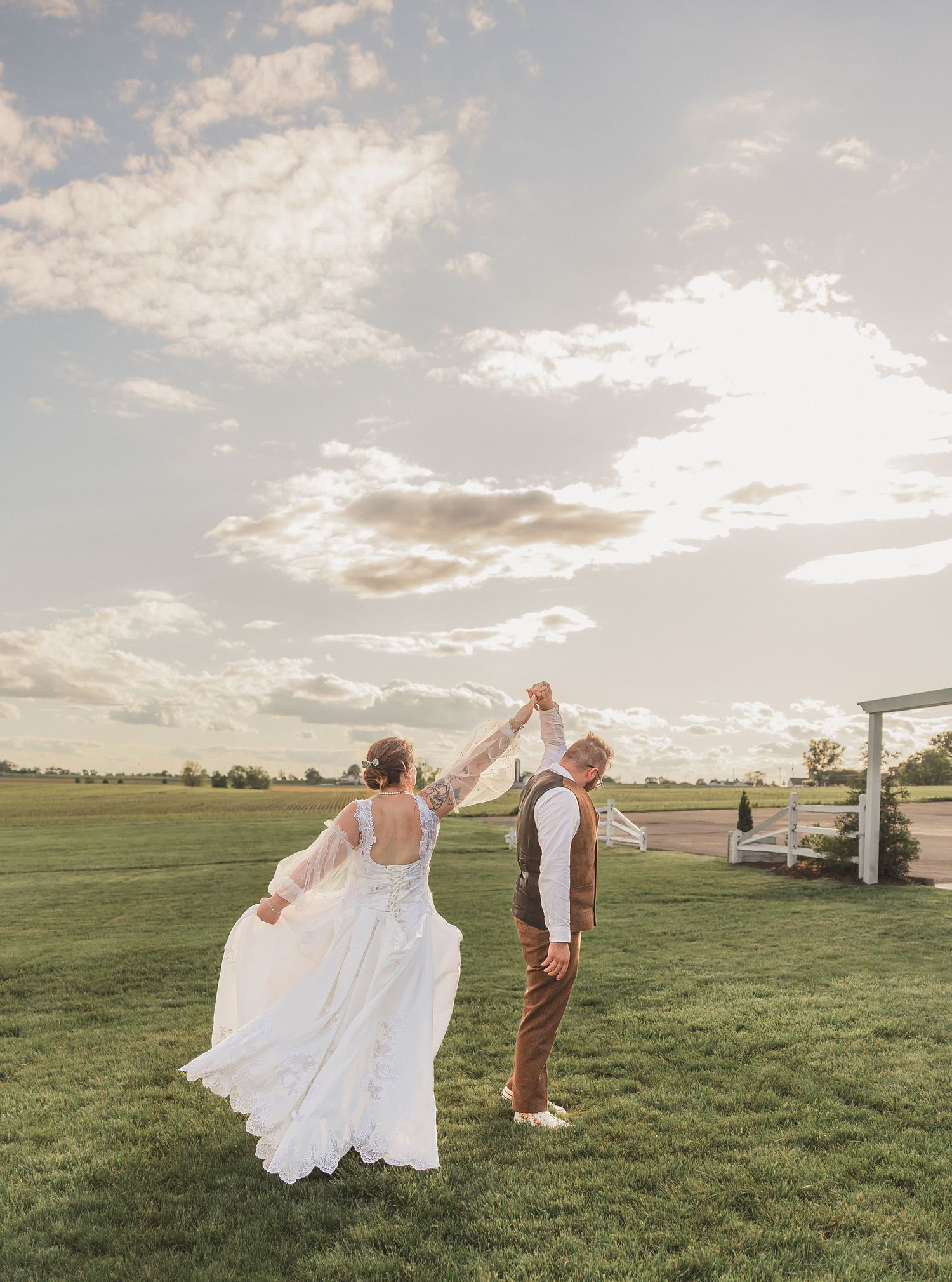 A couple dances joyfully together in a golden green field at sunset, creating a romantic outdoor moment.