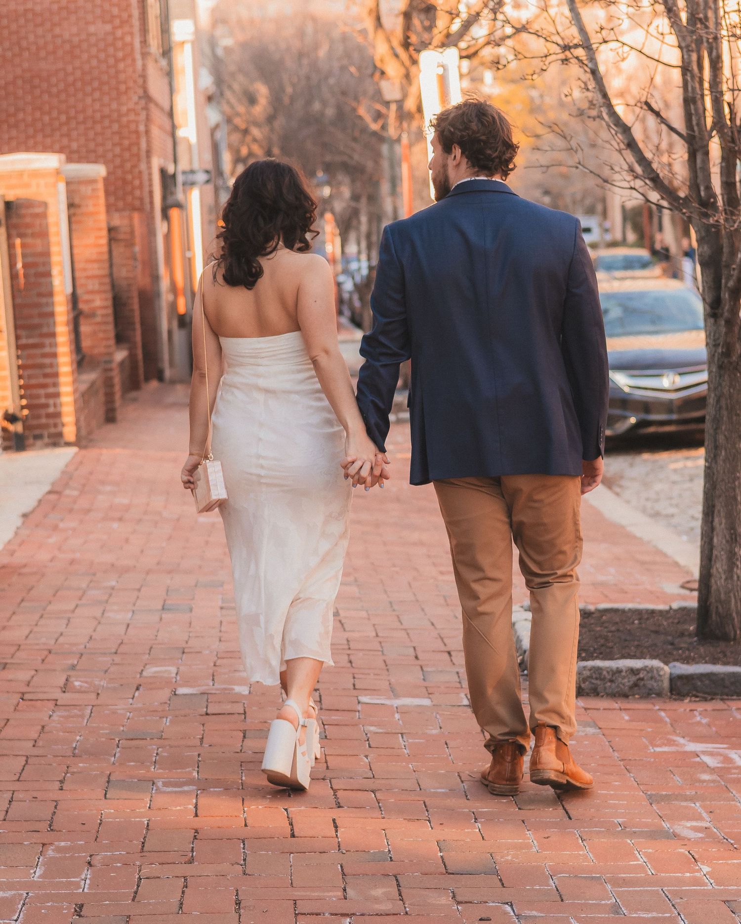 A couple walks hand in hand down a brick-lined street during sunset.