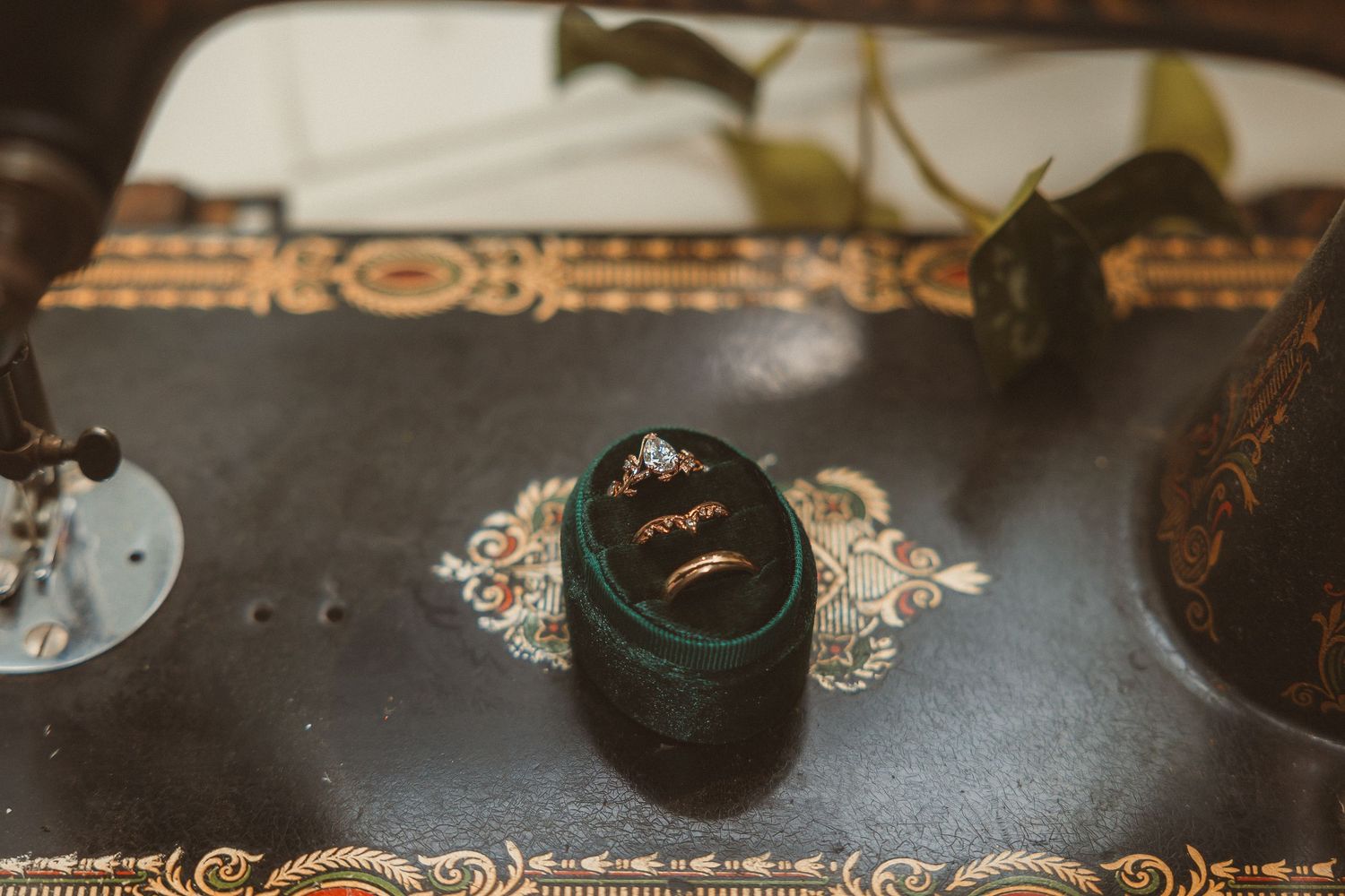 A vintage dark green velvet ring box with ornate metallic decorative details sits on a textured surface.