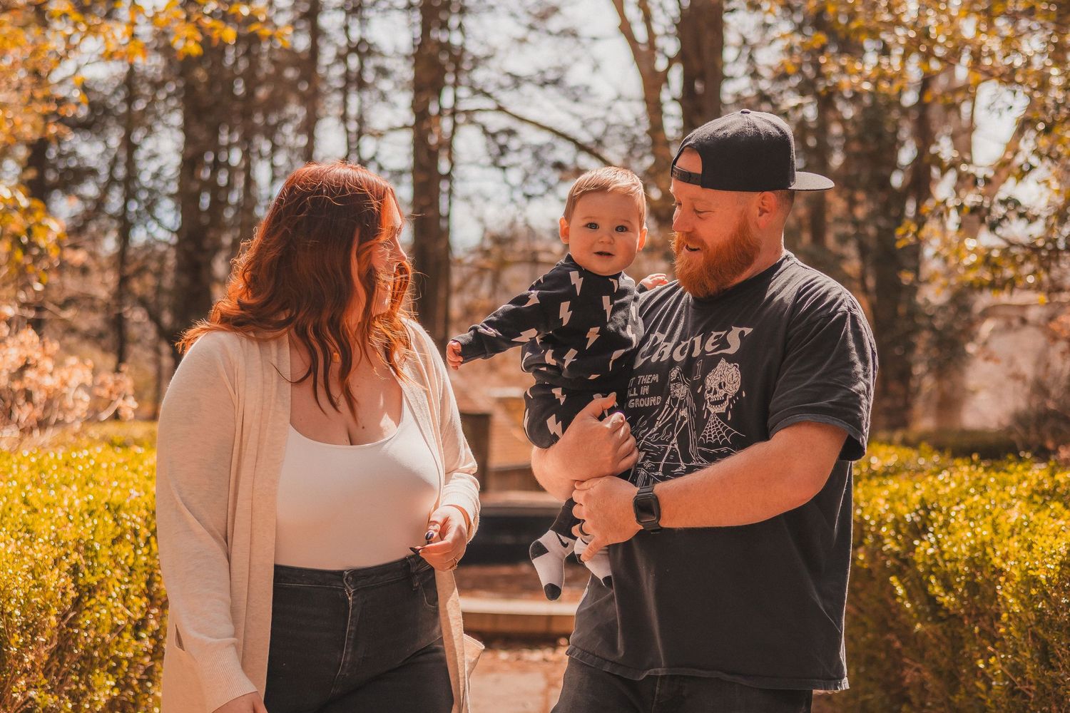 A family enjoying a sunny autumn day together outdoors with fall foliage in the background.
