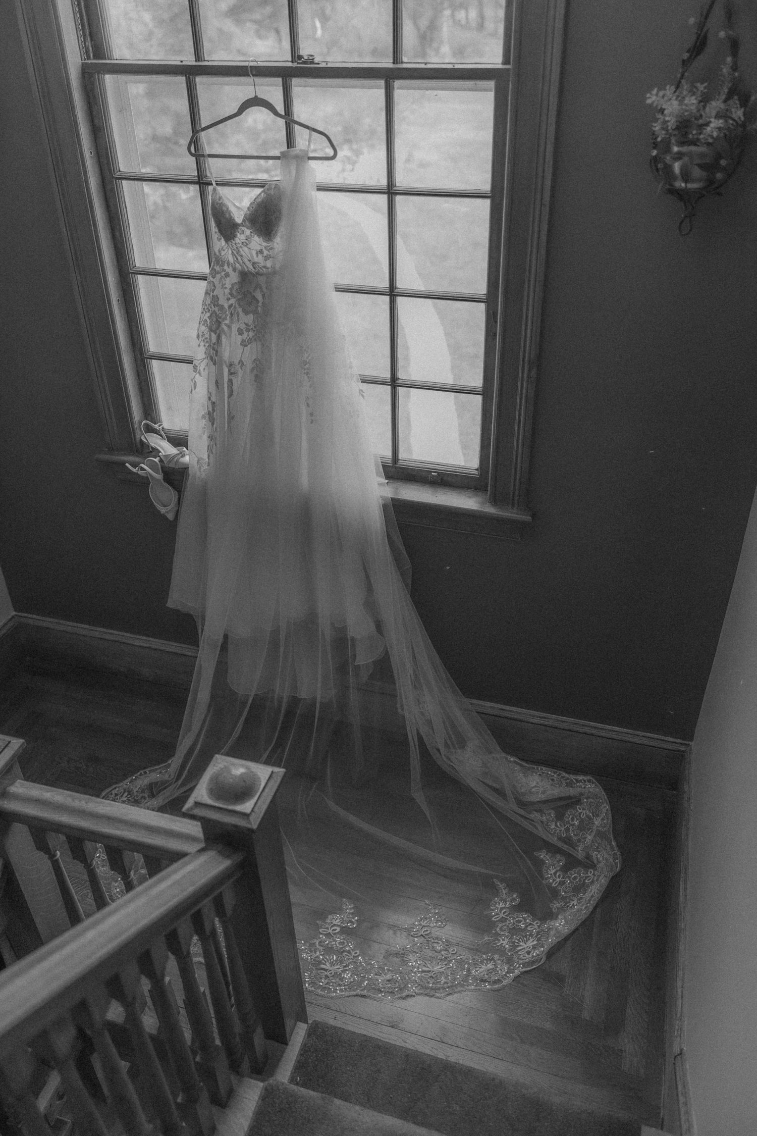 Elegant white wedding dress with long train hanging by window in black and white photography.