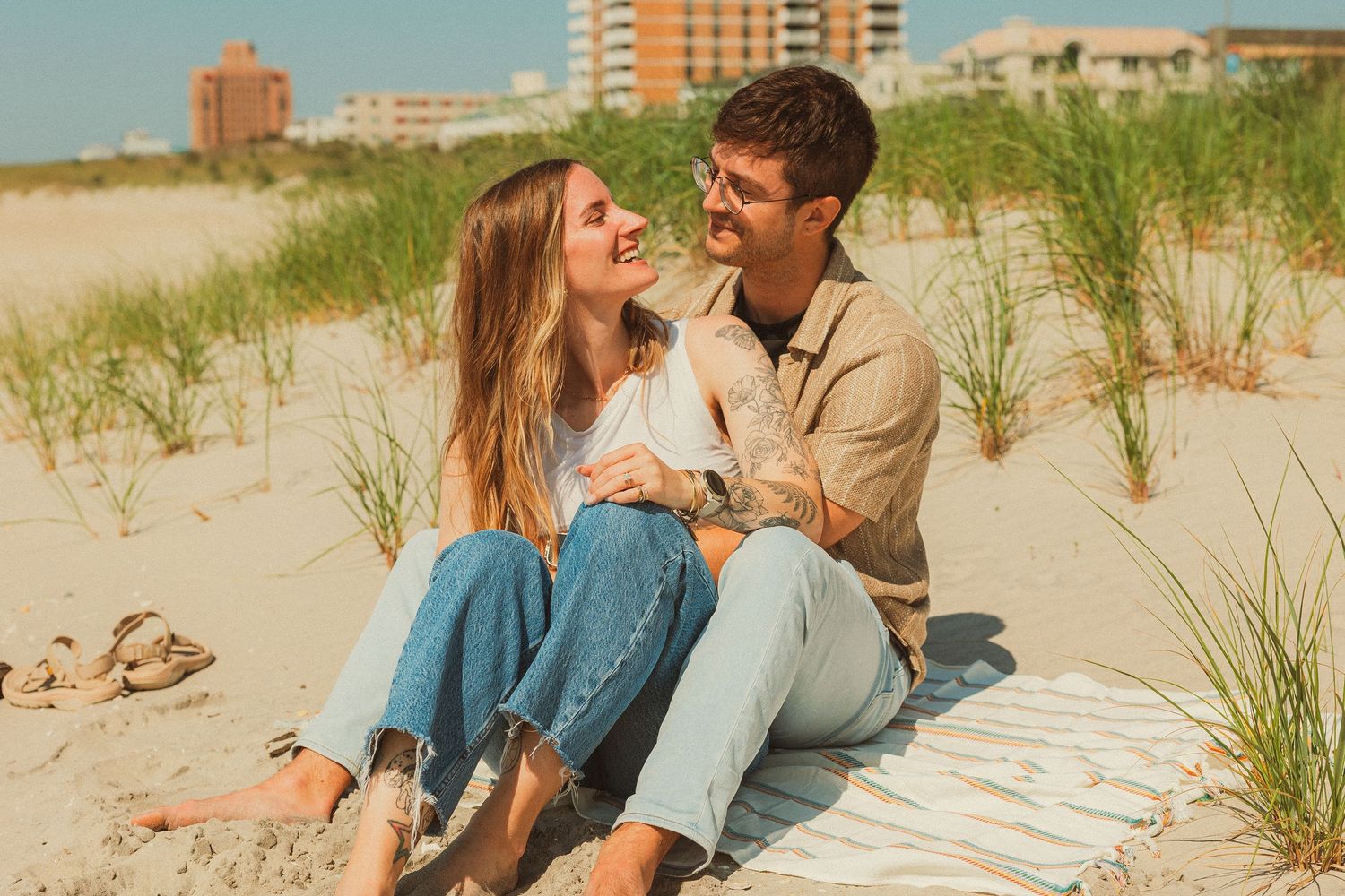 Romantic couple shares intimate moments at the beach while sitting together on a blanket in the sand and dunes.