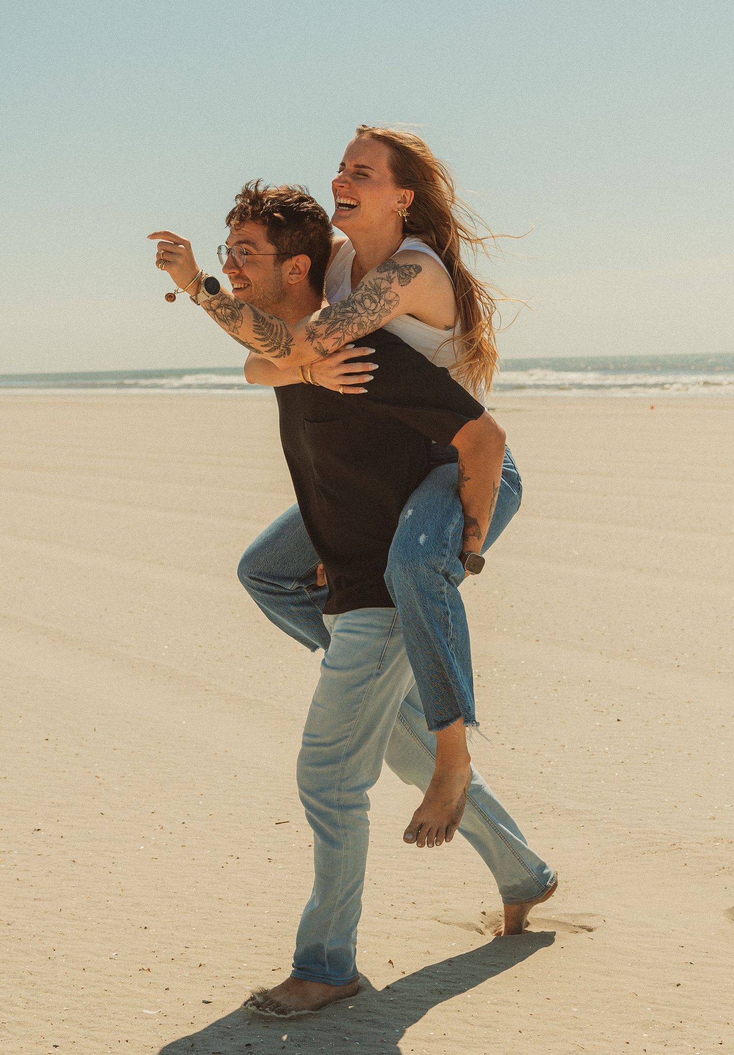 Two friends playfully dancing and spinning together on a sunny beach with waves in the background.