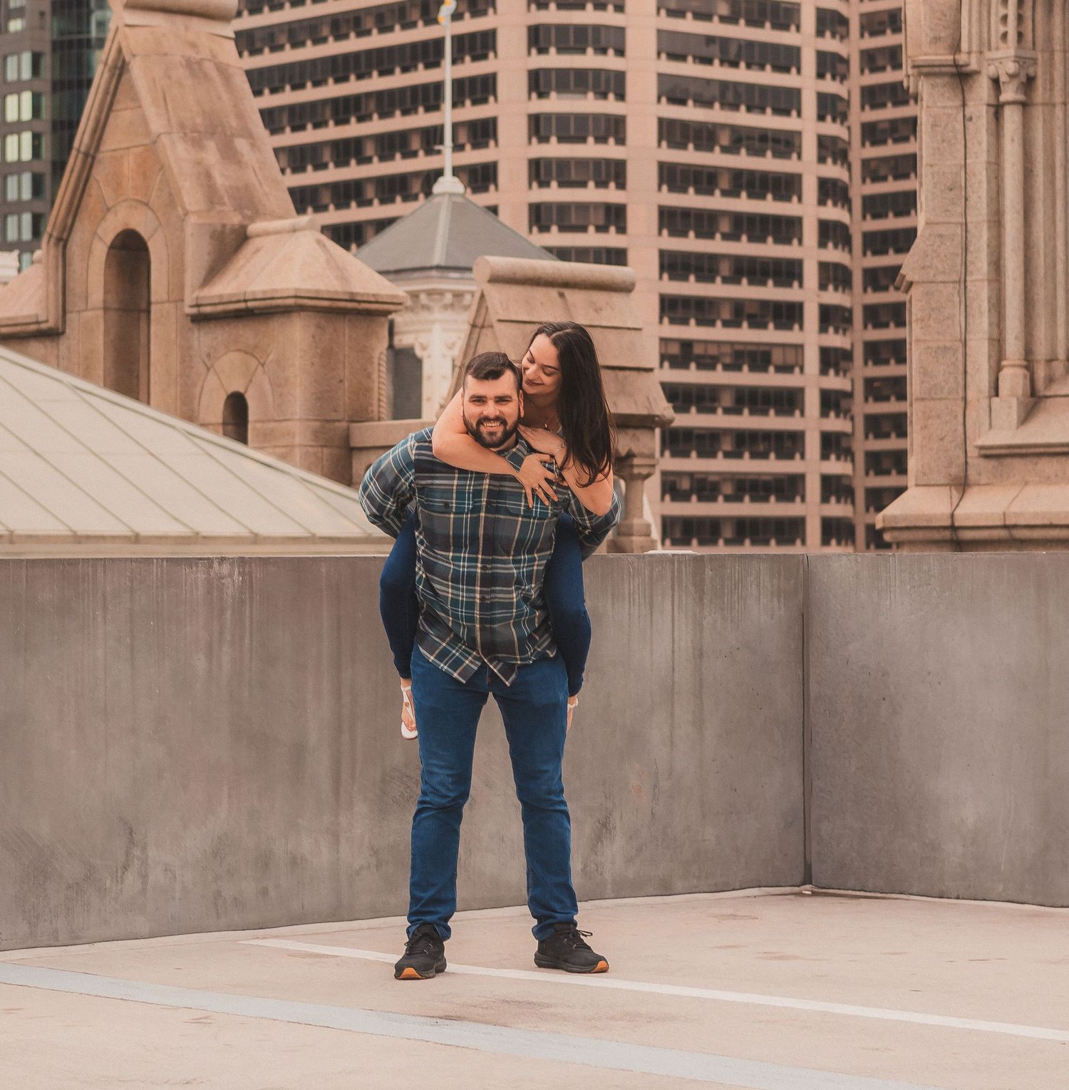 A couple sharing a playful moment on a city rooftop with architectural details visible.