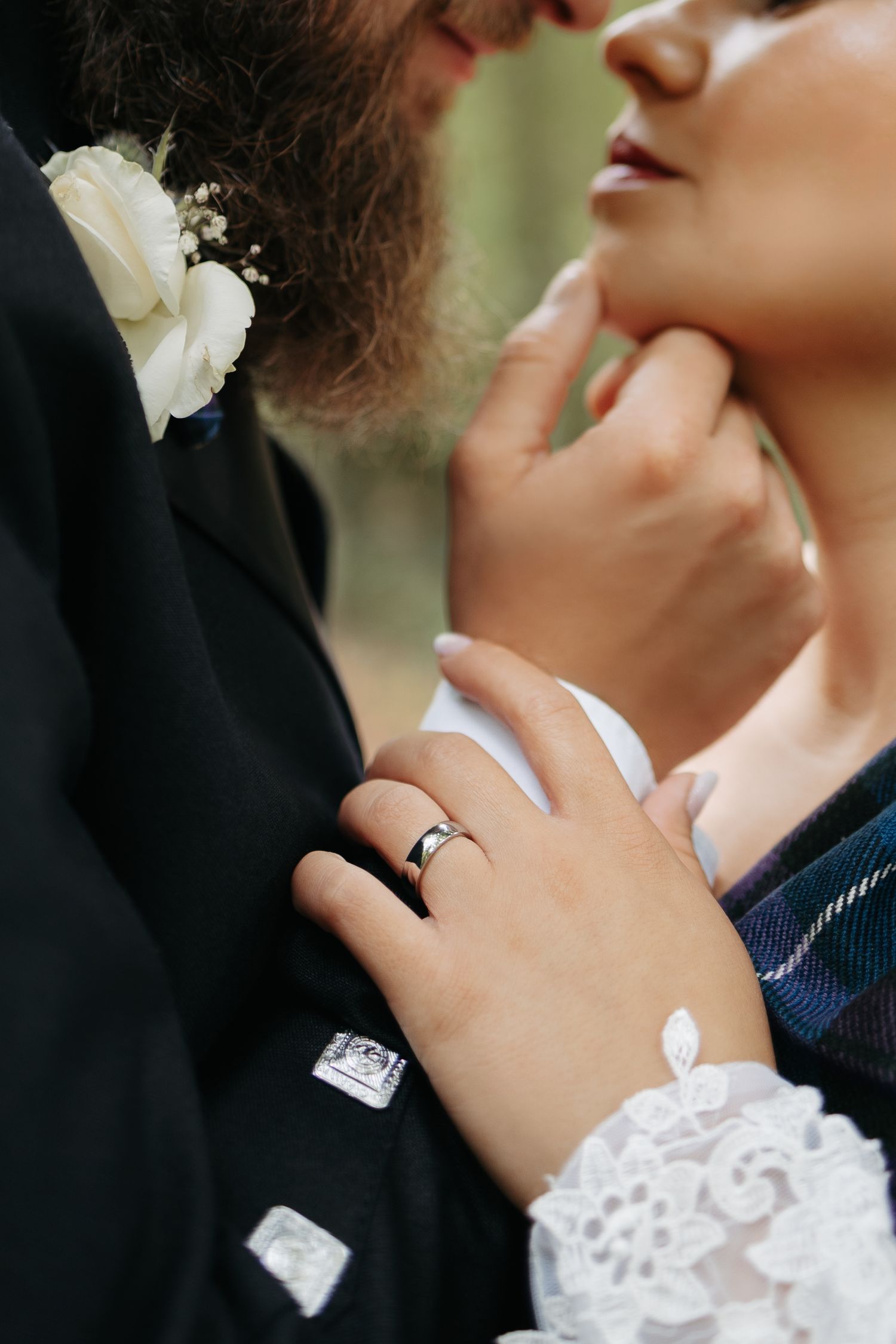 Close-up romantic wedding photo showing a couple's tender embrace with white lace sleeve details and rings visible.