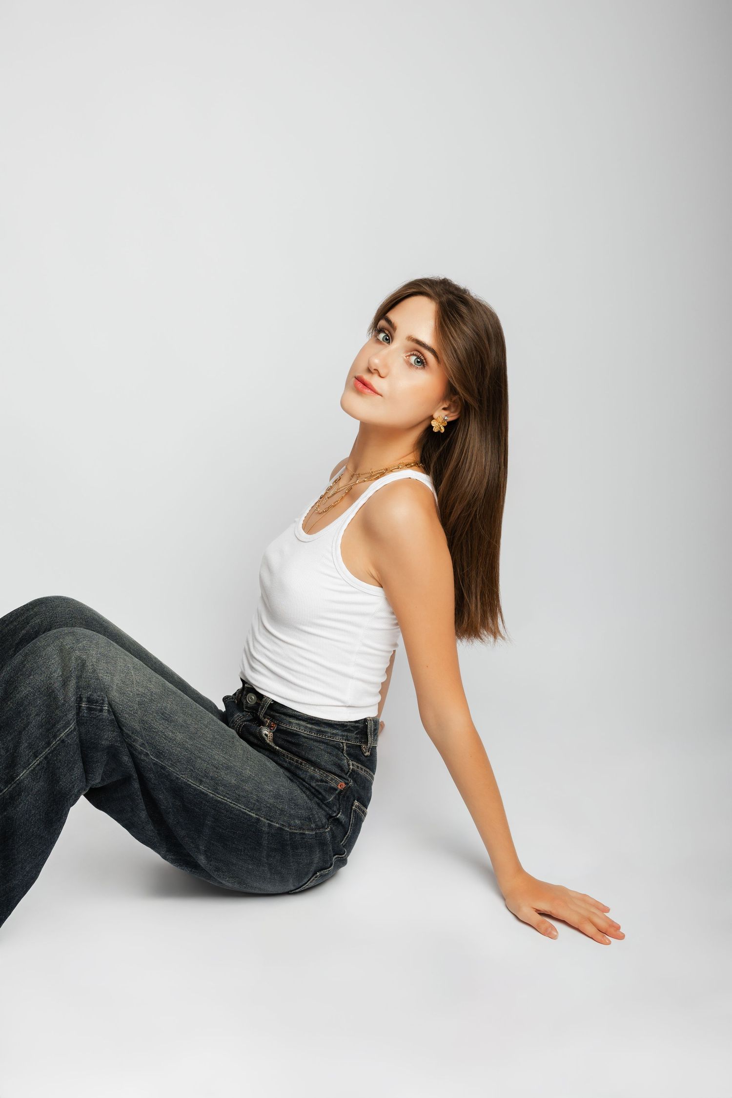 Person in white tank top and jeans poses against white background in artistic fashion photography series.
