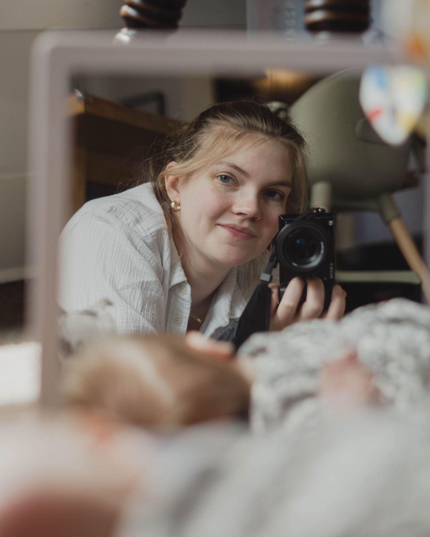Self-portrait taken in a mirror, while lying on the ground. My infant daughter is visible and blurred out in the foreground.