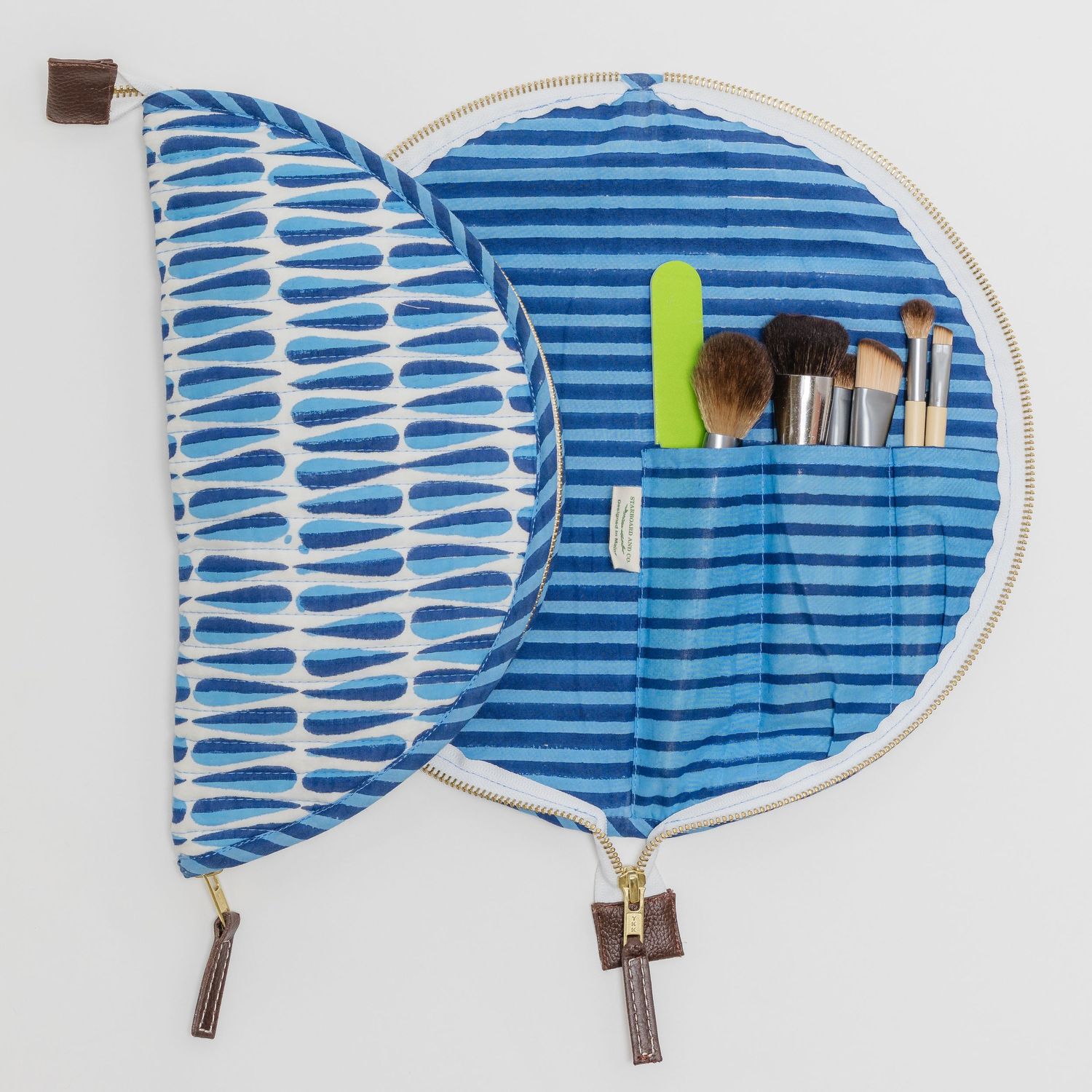 Blue striped circular makeup organizer bag open displaying makeup brushes and tools in interior pockets.