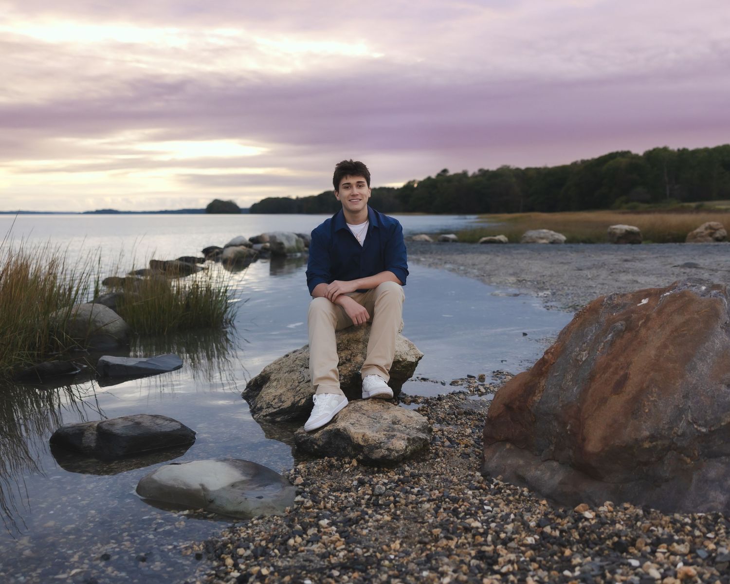 Southern Maine Senior Portrait Photographer - Person sits on rocky shore beside ocean at dusk.