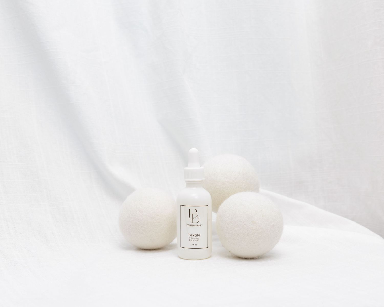 White wool dryer balls with a spray bottle of laundry scent on a soft white fabric background.