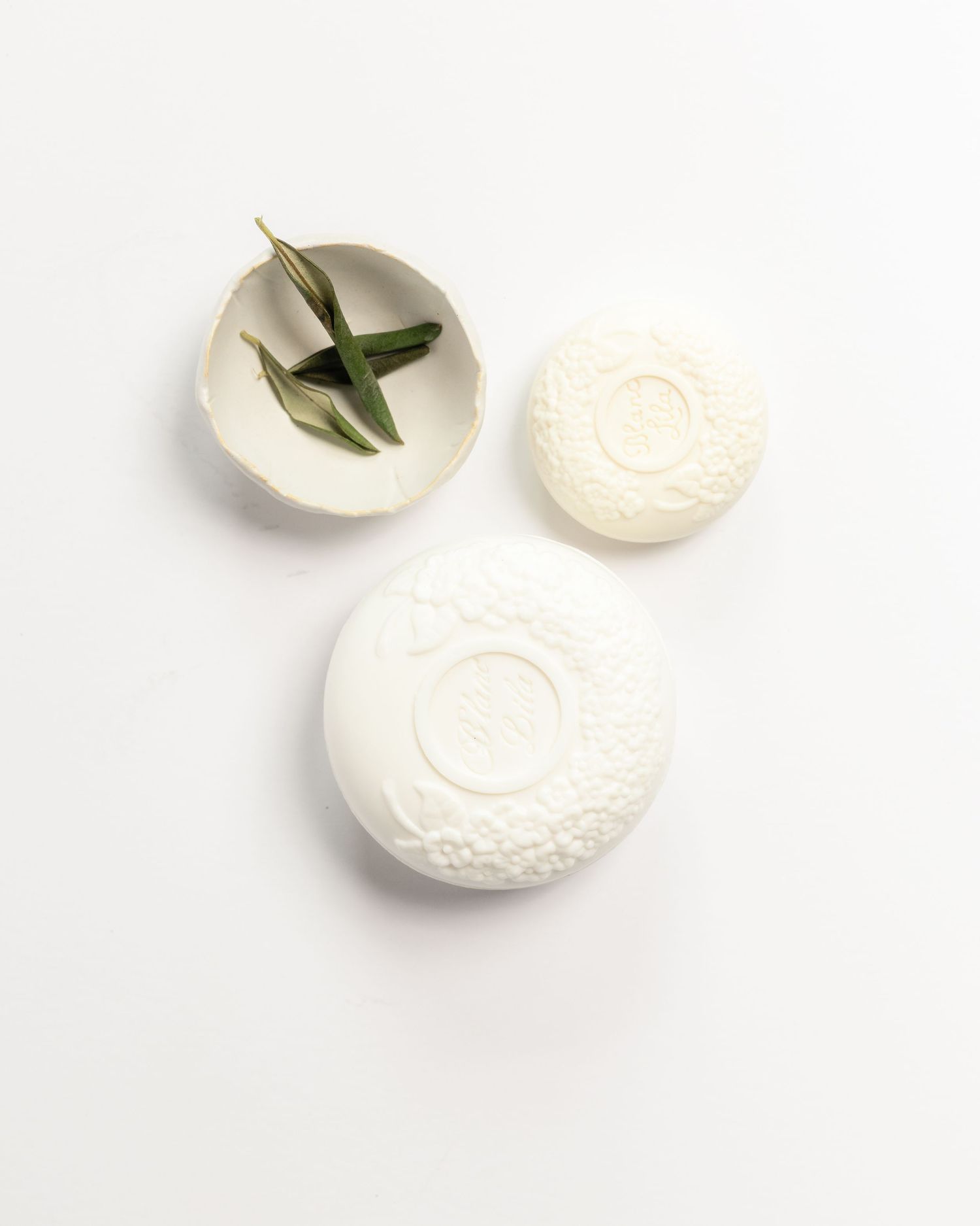 white embossed oval soaps beside a ceramic dish with olive branches, product photography by Portland Maine photographer Ang Foley
