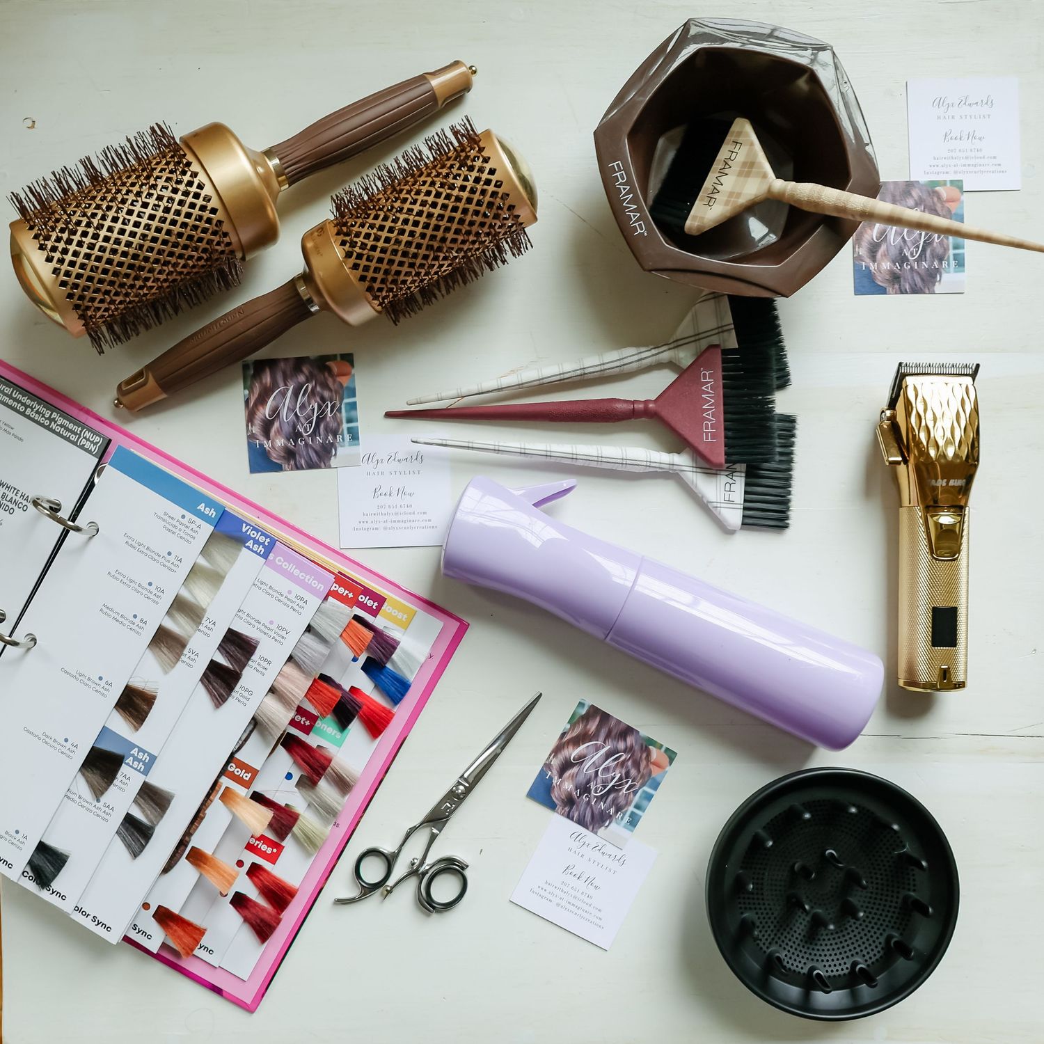 Hairdressing tools including round brushes, scissors, hair clippers, dye bowl, color chart, and a purple hair dryer on a white surface.