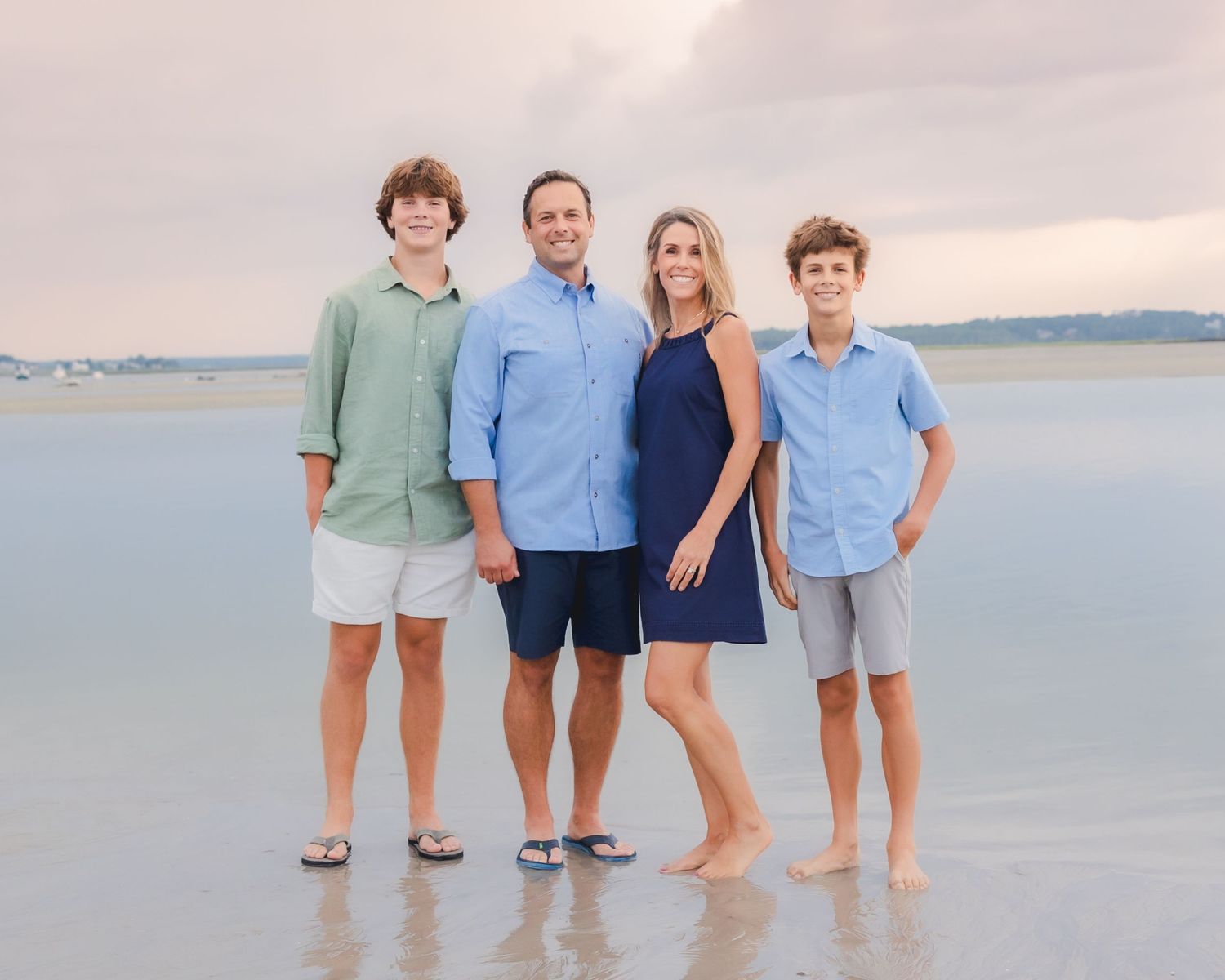 Southern Maine Family Portrait Photographer - Family of four poses together on beach at sunset in coordinated casual outfits.