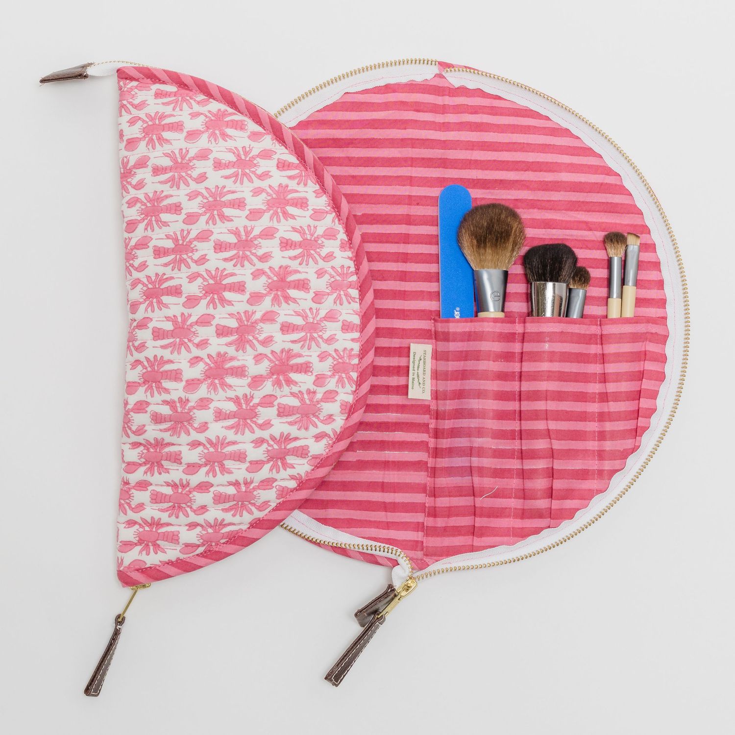 Pink striped round makeup bag open displaying brushes in pockets, with floral print interior lid.