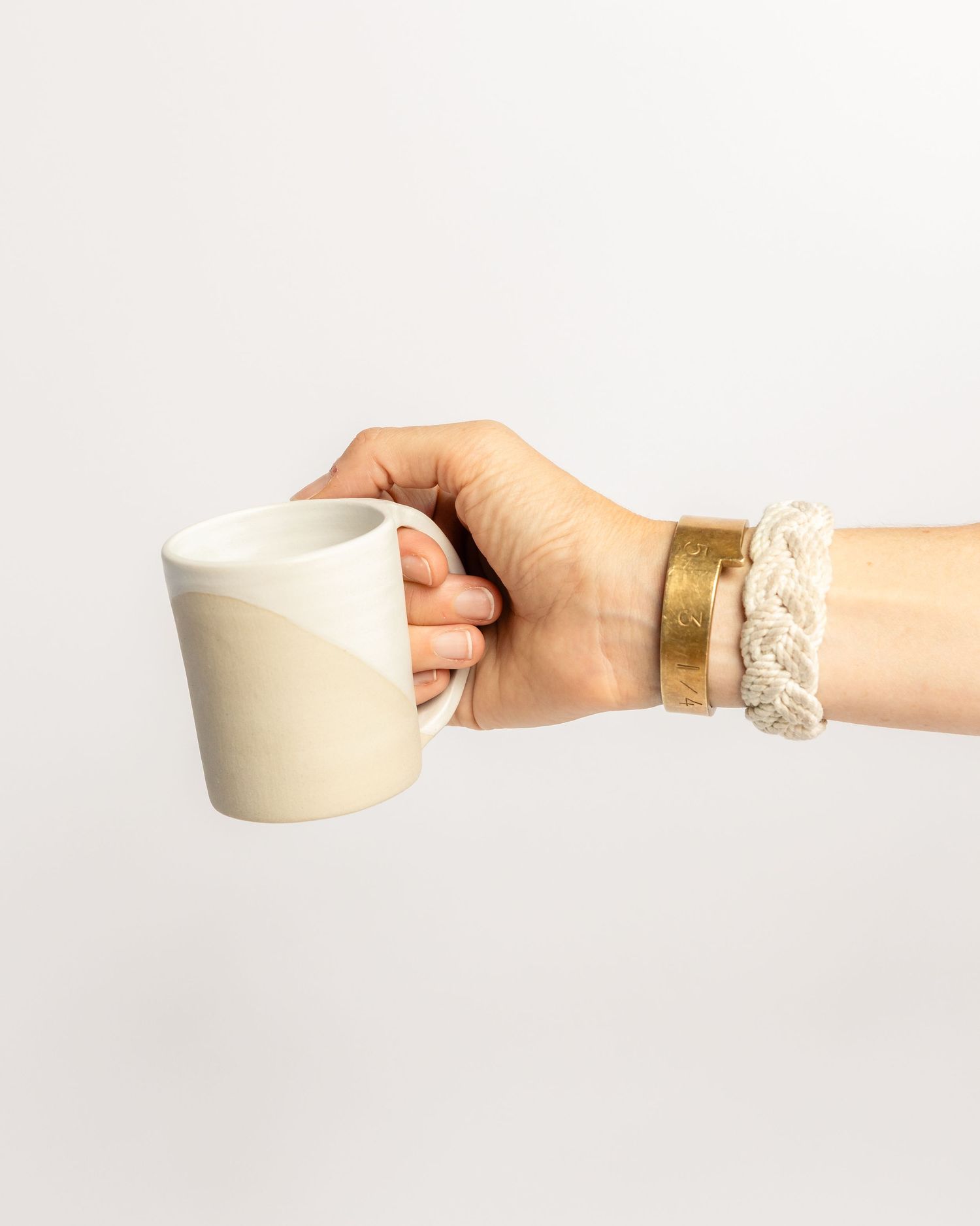 Two-tone white and cream ceramic mug, with gold and macrame bracelets on wrist, product photography by Portland Maine photographer Ang Foley