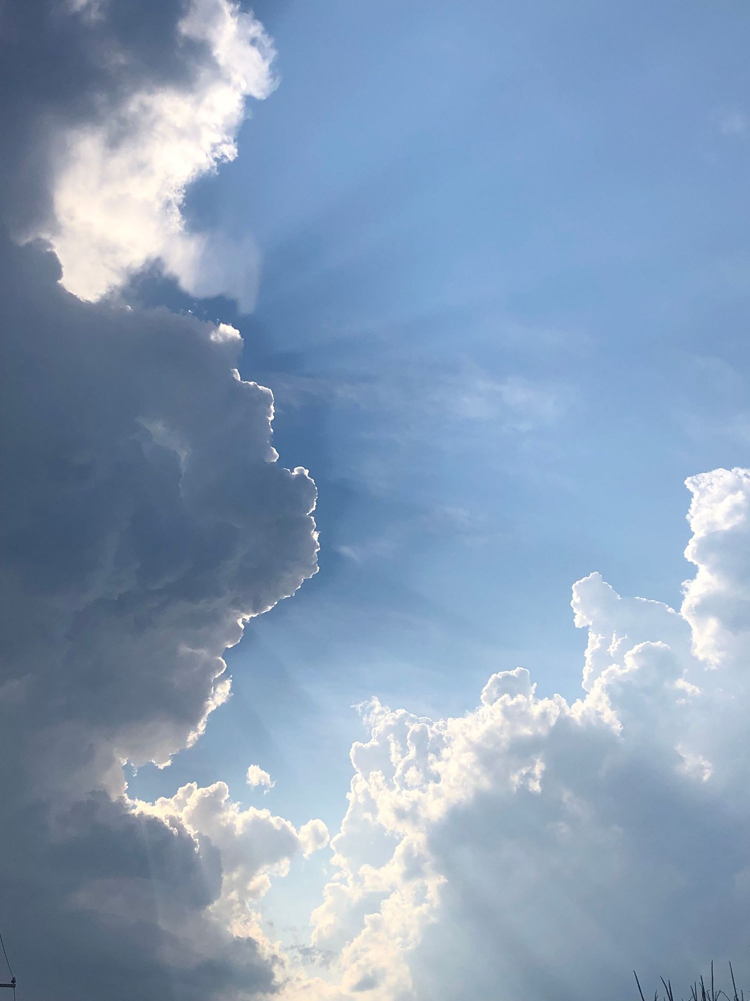 Dramatic blue sky with billowing cumulus clouds and sunbeams radiating through gaps, creating a celestial light effect.