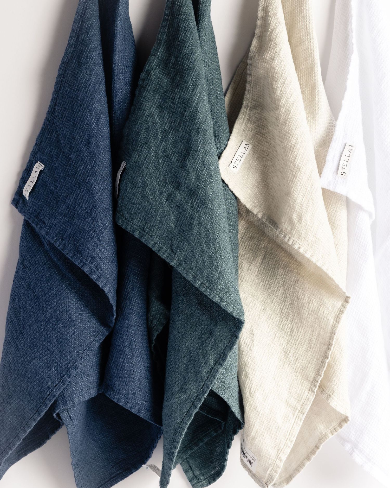 Four linen kitchen towels in navy, dark green, natural, and white, product photography by Portland Maine photographer Ang Foley