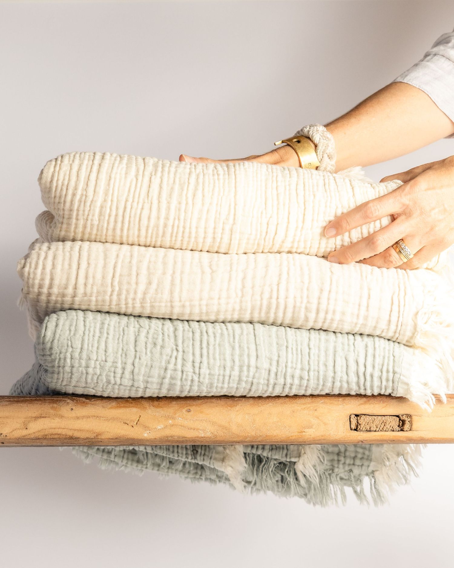 Folded cream and sage green cotton muslin blankets on a rustic wooden shelf, product photography by Portland Maine photographer Ang Foley