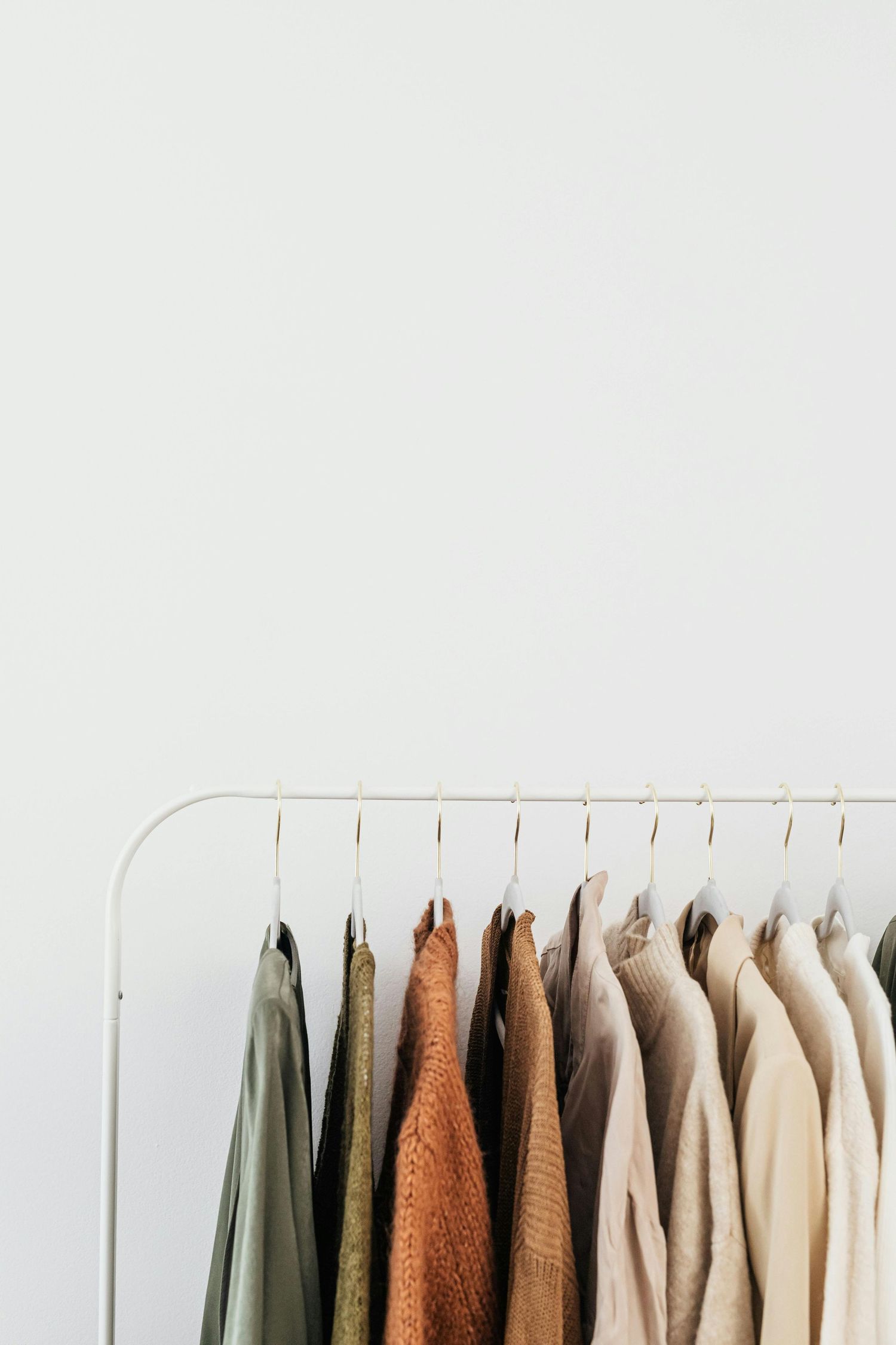 Neutral toned clothes hanging on a minimalist white clothing rack against a light gray wall.