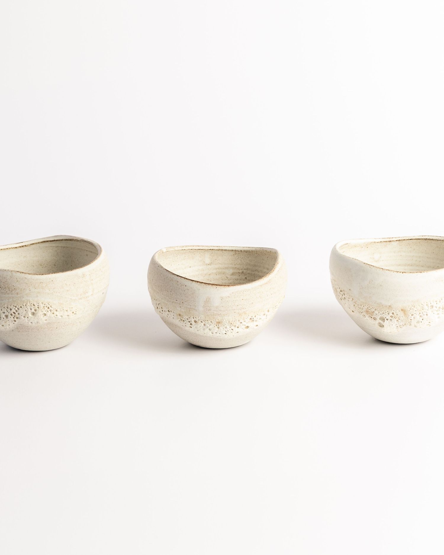 White ceramic bowls with textured speckled finish arranged in a row, product photography by Portland Maine photographer Ang Foley