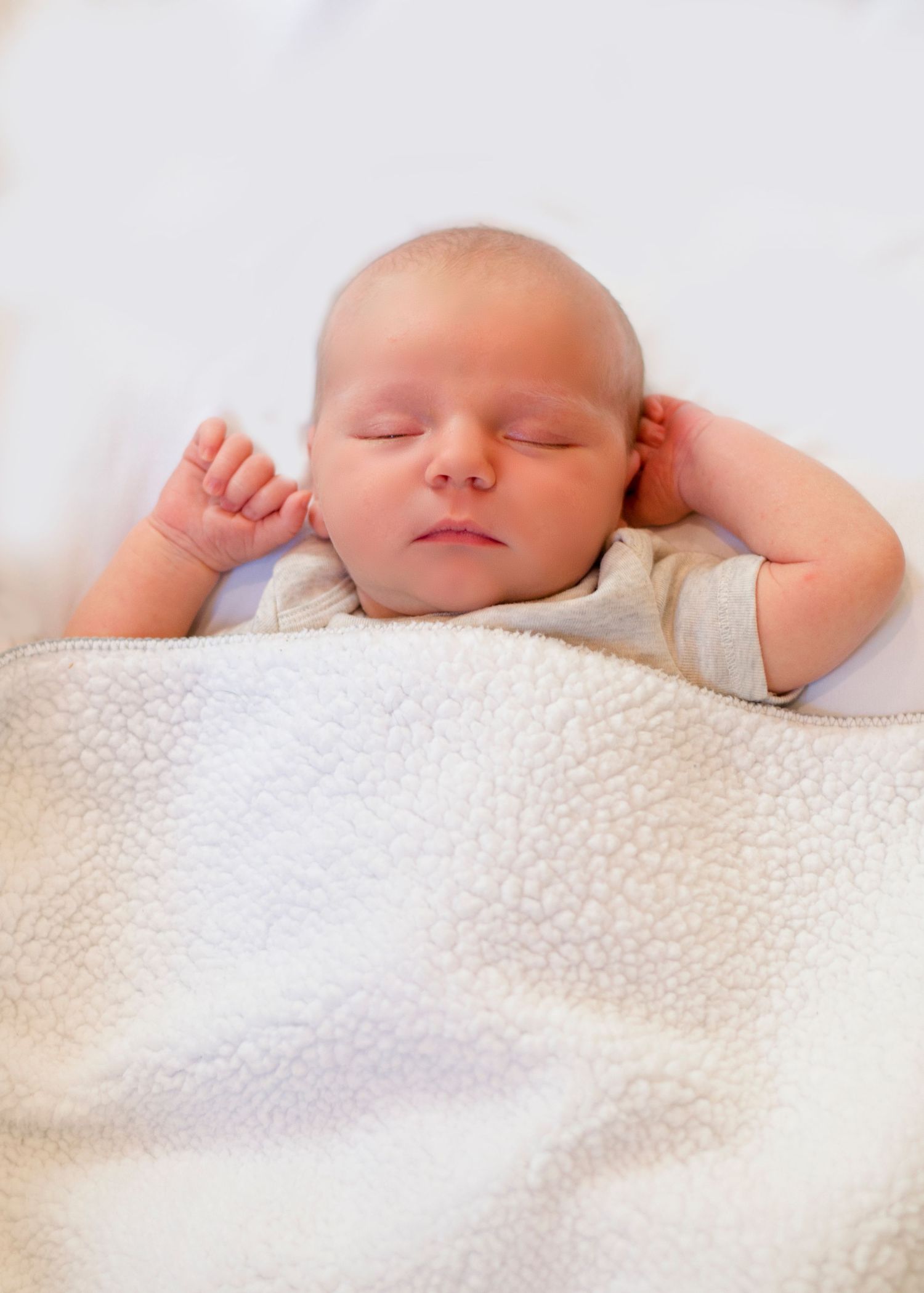 Sleeping newborn with peaceful expression on white blanket.